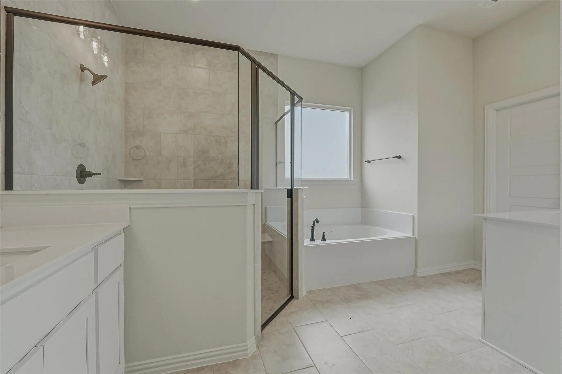 Spacious bathroom featuring a glass-enclosed shower with tile surround, a built-in soaking tub, a single vanity with stone countertop, and light-toned tile flooring