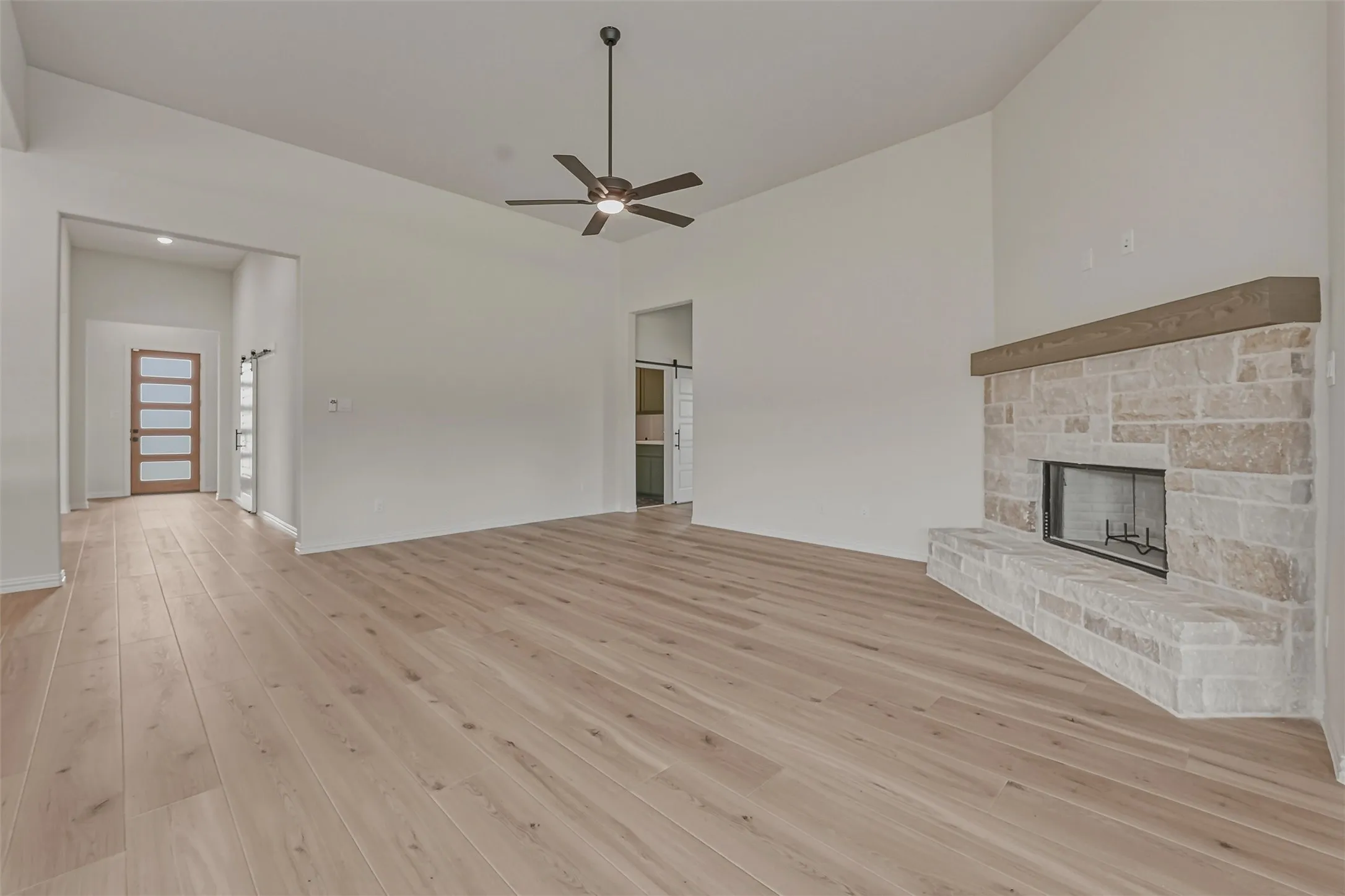 Spacious living area featuring wood-finish flooring, a vaulted ceiling with a ceiling fan, and a stone fireplace with a wood mantle