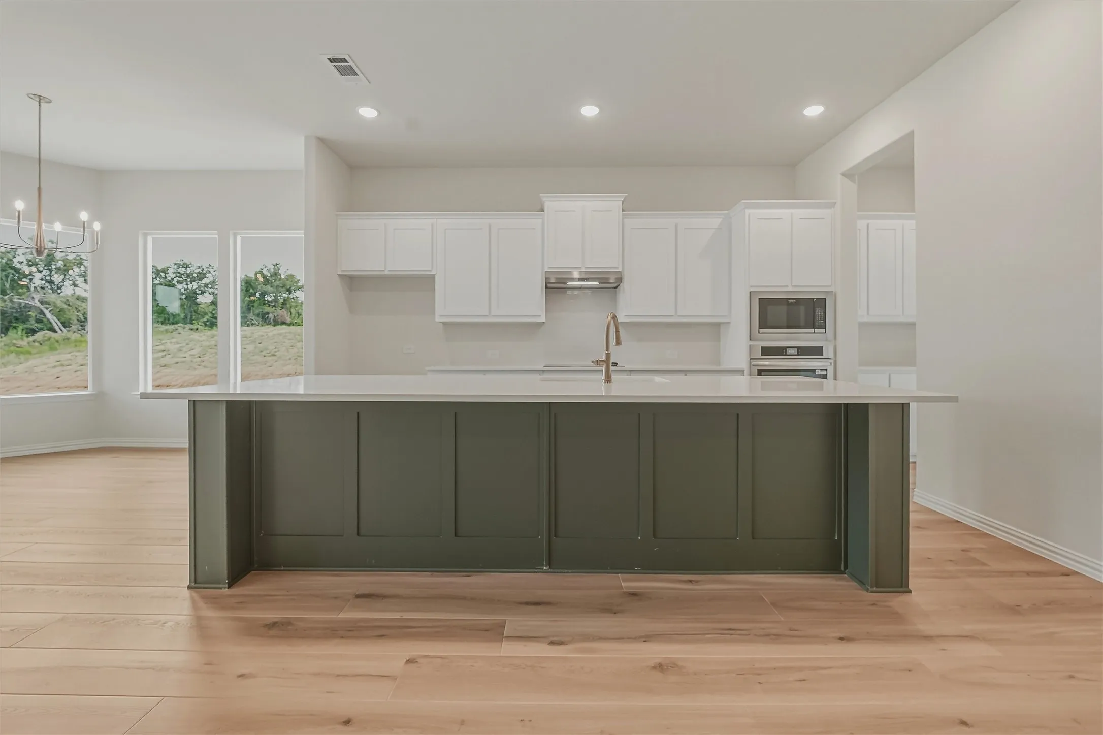 Kitchen island featuring a dark green panel base, light-toned countertop, and brass-finish faucet