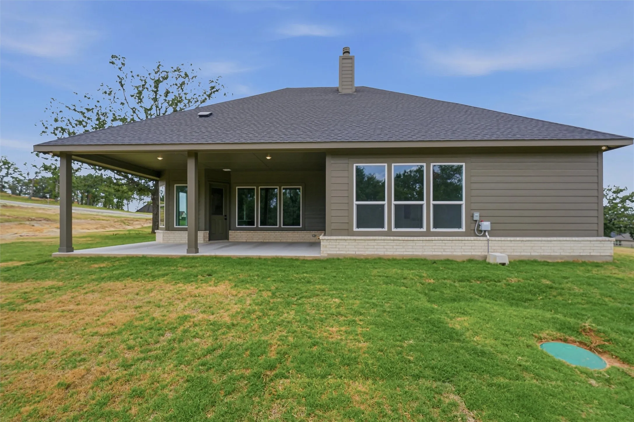 Rear exterior featuring a covered patio, multiple windows, a grey shingle roof, and a stone-clad foundation
