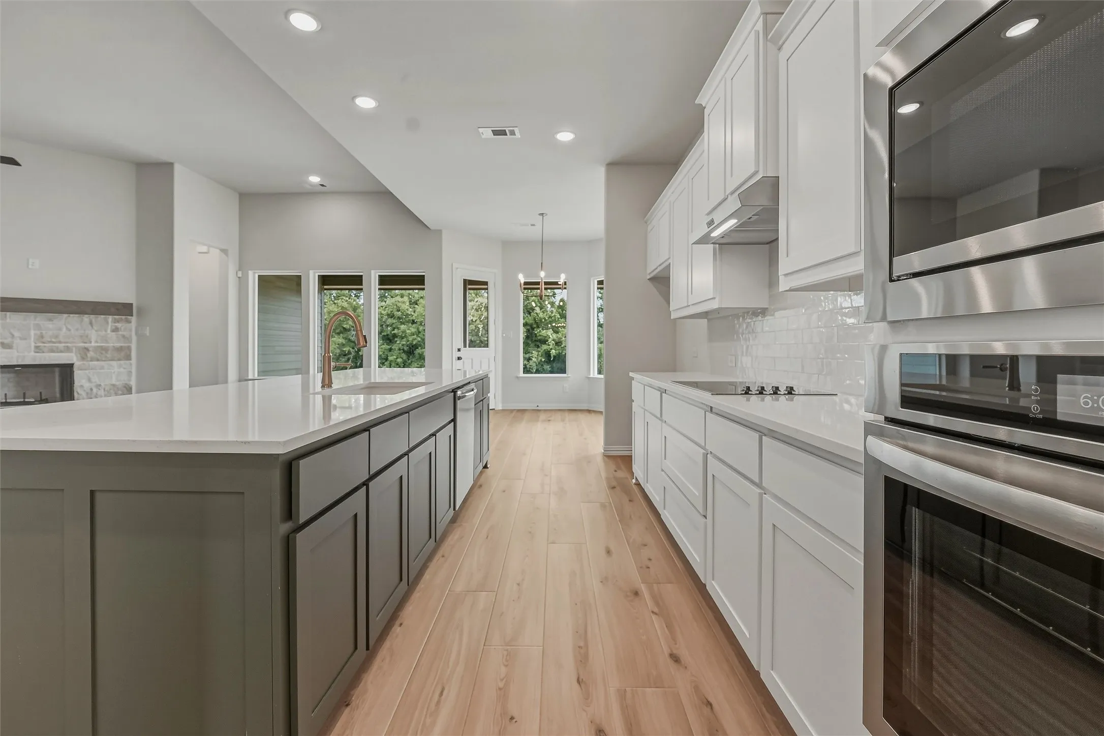 Kitchen featuring a substantial central island with a sink and a contemporary faucet, light wood-finish flooring, white cabinetry, integrated stainless steel appliances, and a subway tile backsplash