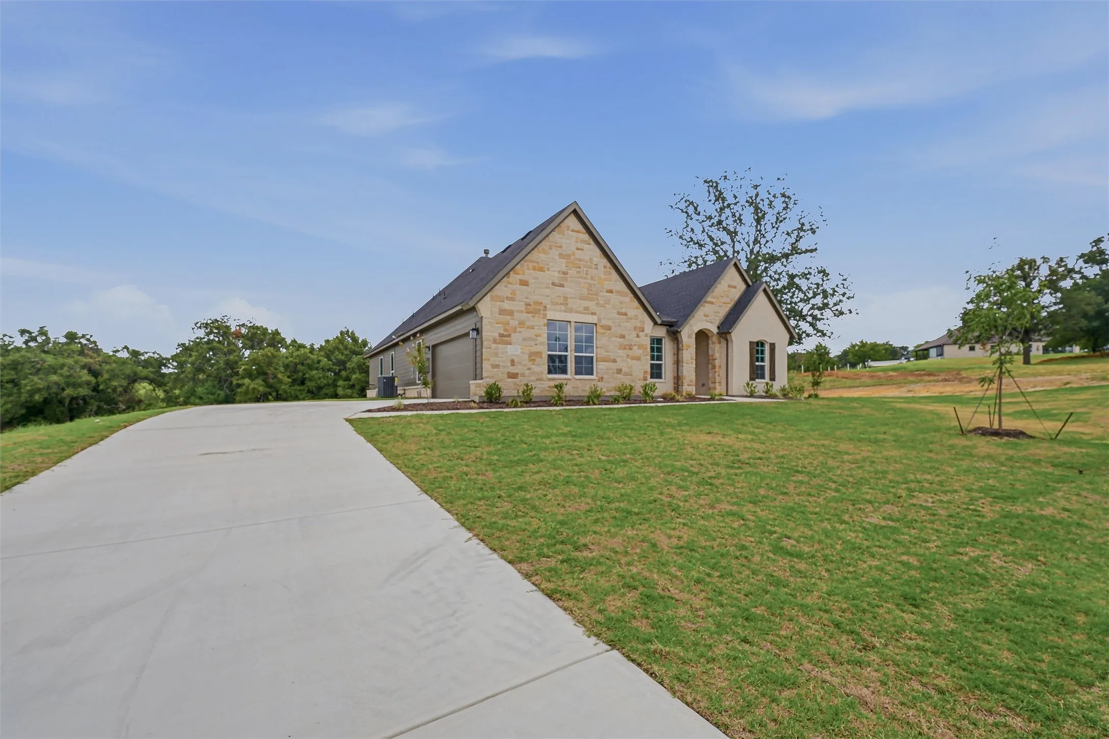 Stone veneer exterior with dark shingle roofing and a spacious concrete driveway