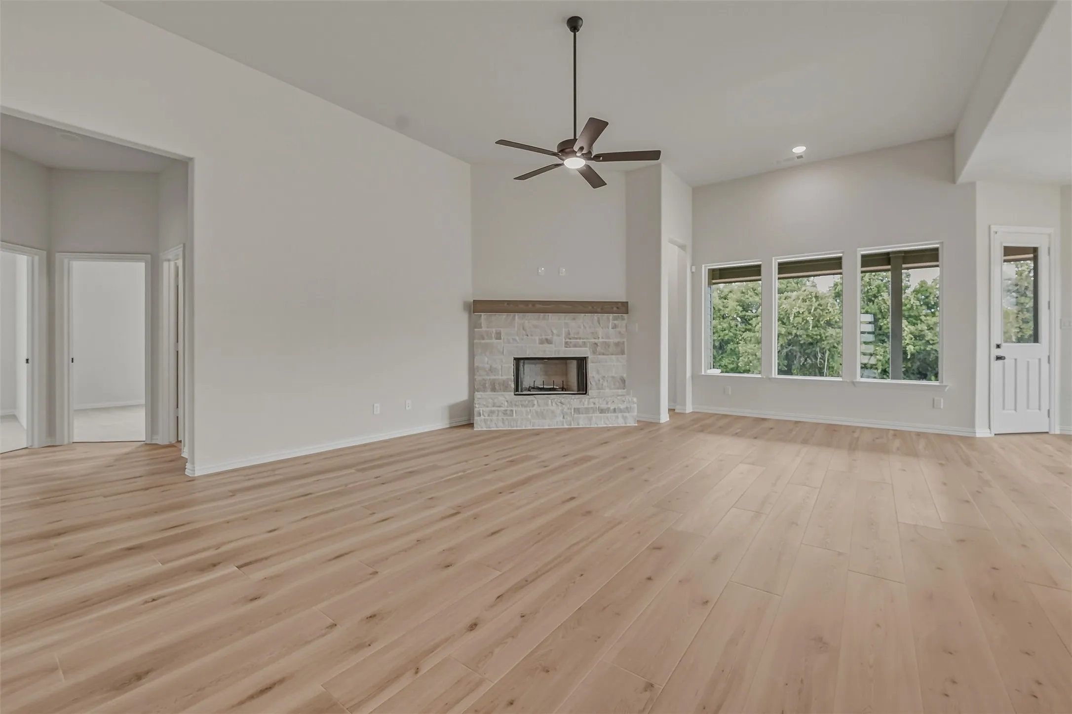 Spacious room featuring wood-finish flooring, a stone fireplace with a wood-finish mantel, vaulted ceilings, and a ceiling fan