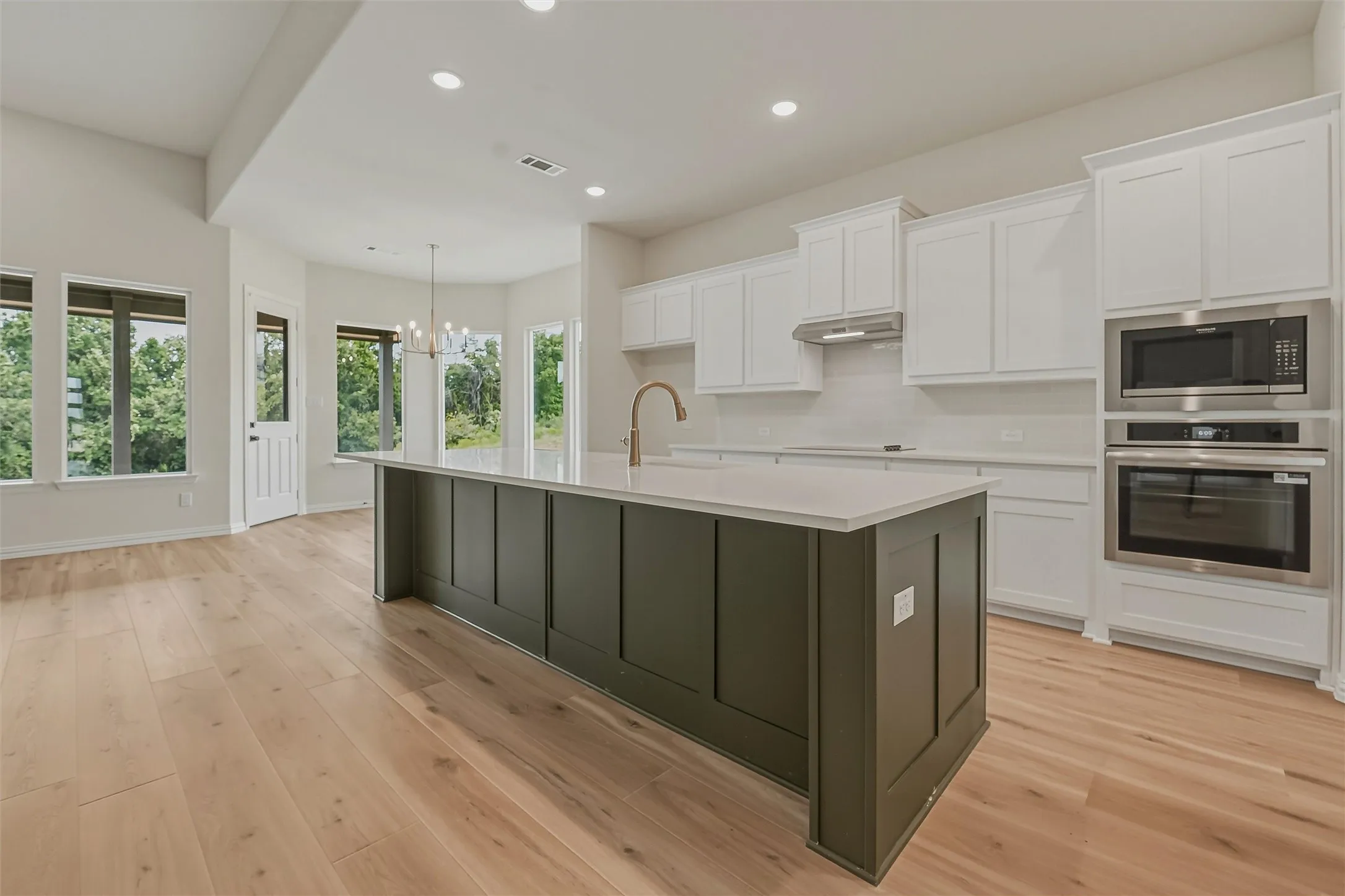 Kitchen featuring a large central island with a dark green panel finish, white perimeter cabinetry, light wood-finish flooring, and stainless steel built-in appliances including a microwave and oven