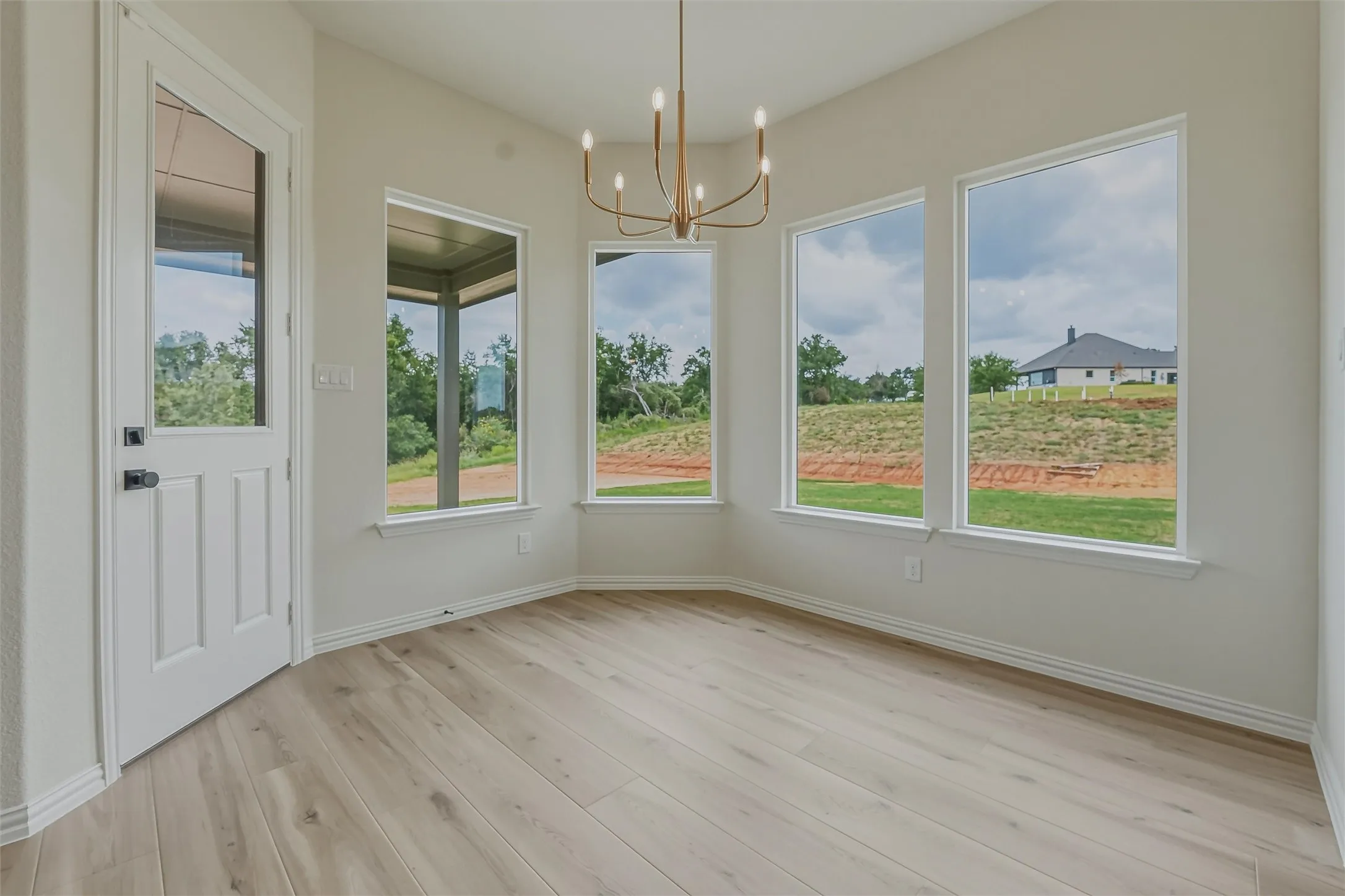Bay window area featuring light wood-finish flooring, a modern brass chandelier, and multiple large windows