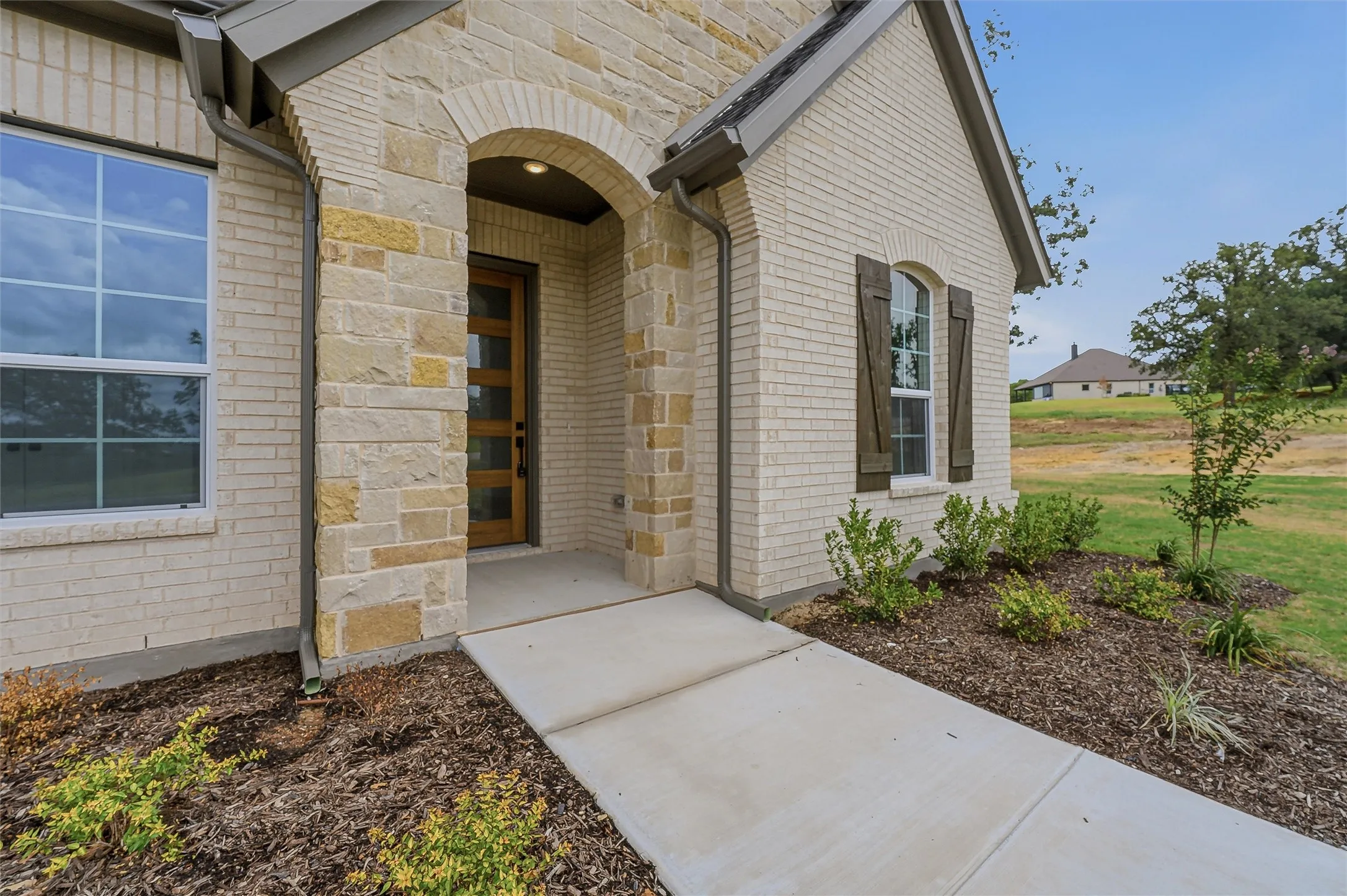 Inviting entryway featuring an arched stone portico, a modern wood-finish door with frosted glass panels, and contrasting light brick siding