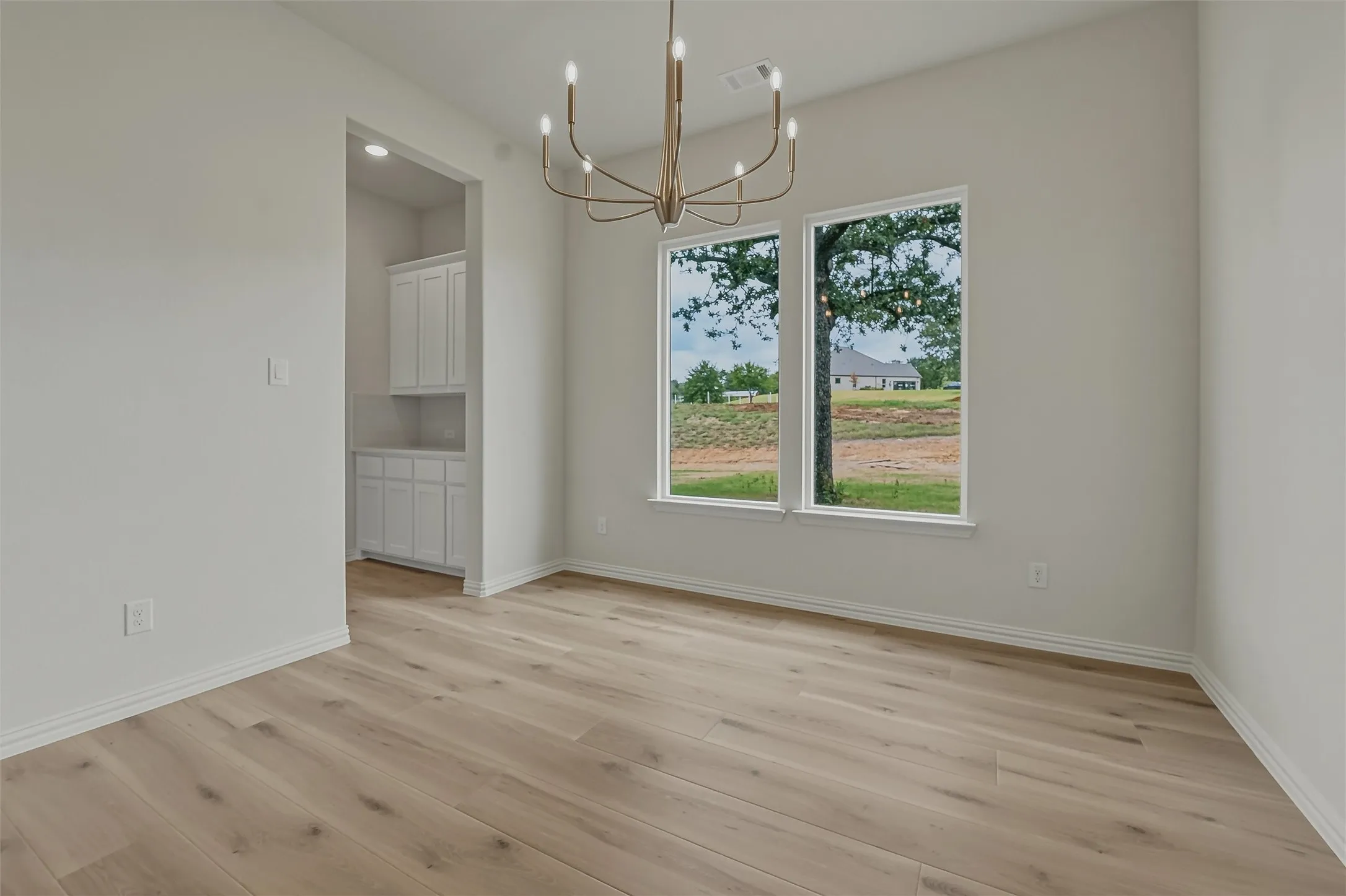 Spacious room featuring light wood-finish flooring, a contemporary bronze chandelier, and dual windows