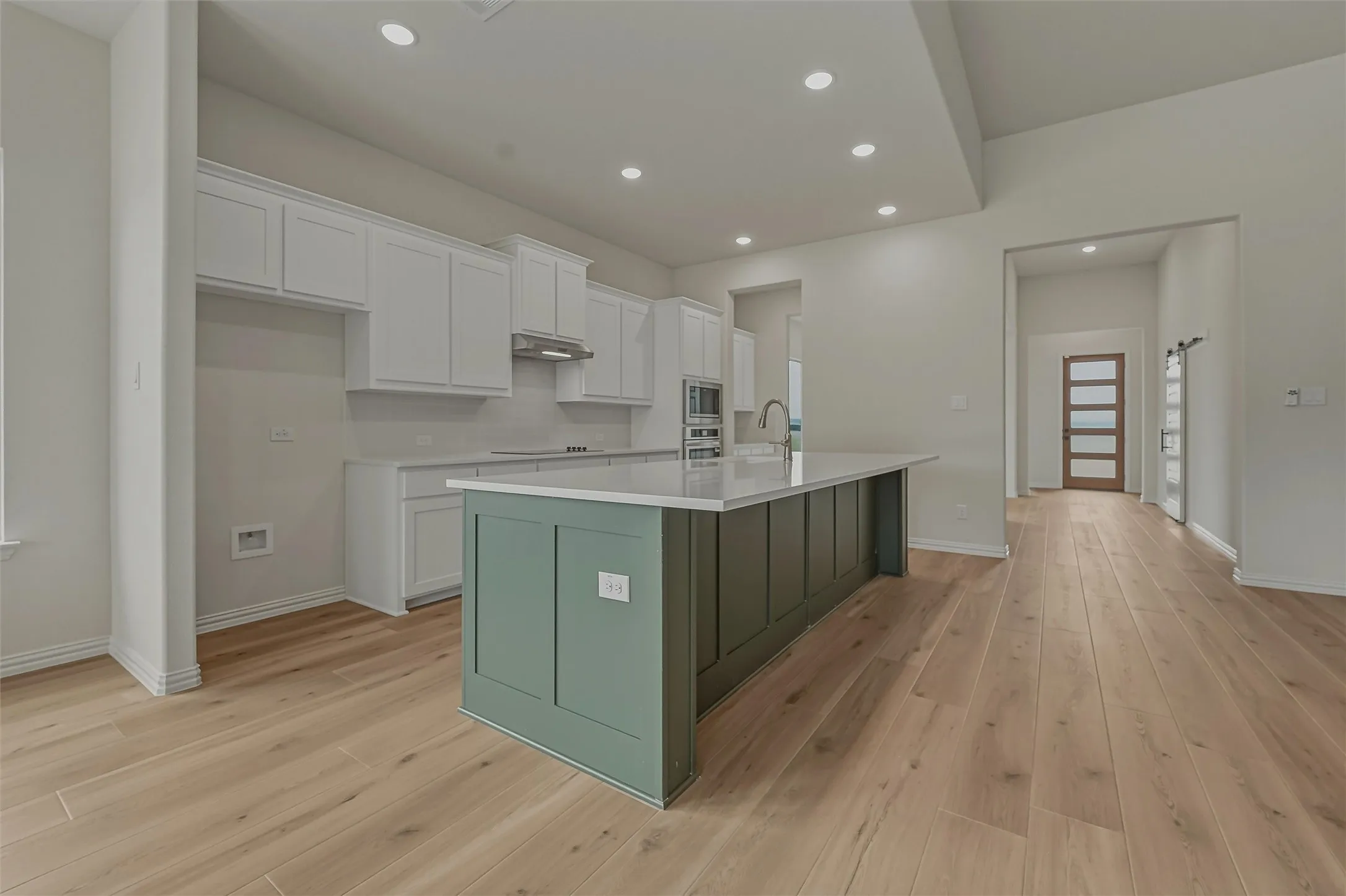 Spacious kitchen featuring an expansive center island with a quartz countertop, white shaker cabinetry, stainless steel appliances, and wood-finish flooring