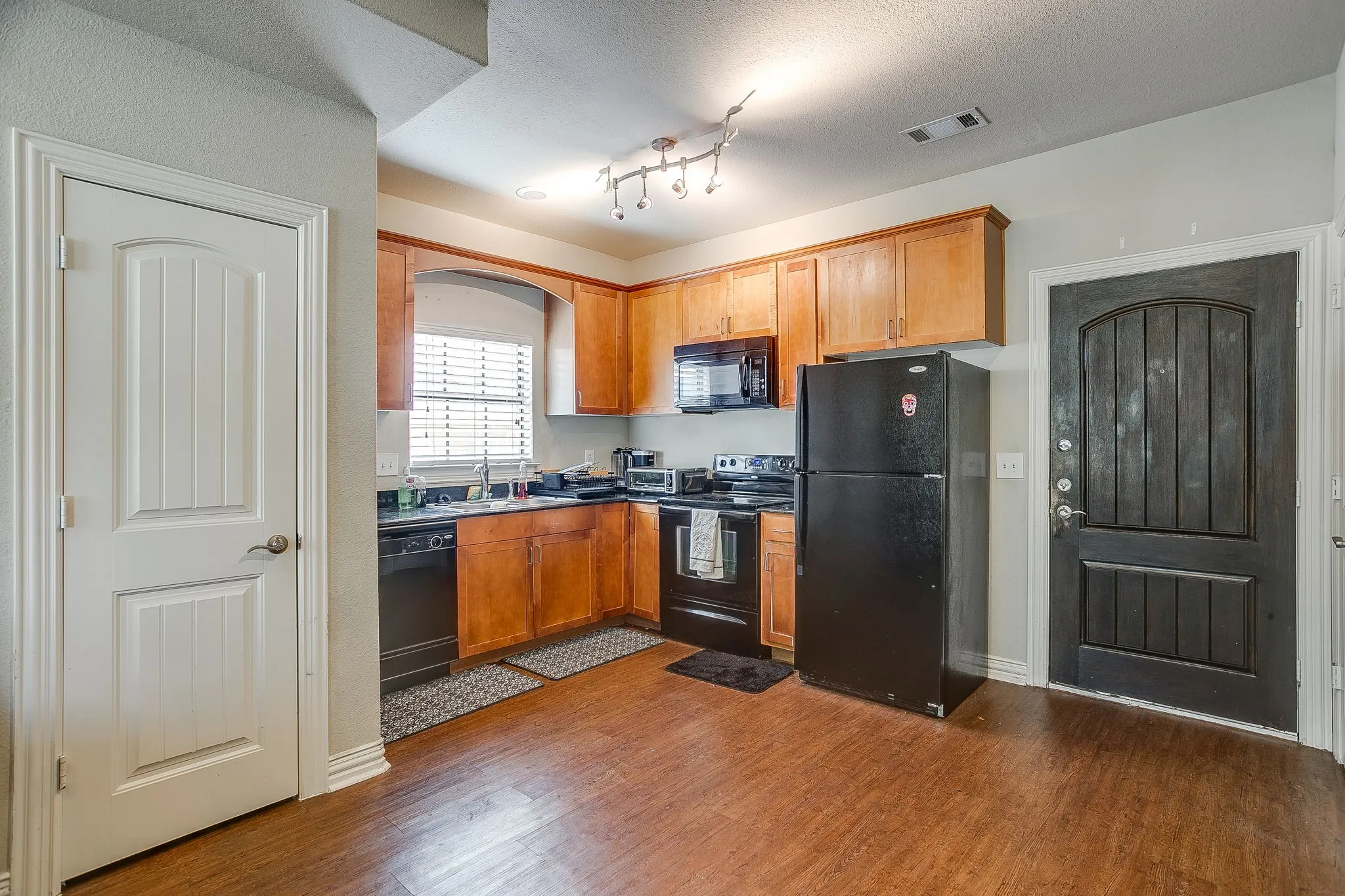 Kitchen with black appliances, wood finish cabinets, dark wood-style flooring, a textured ceiling, and dark countertops