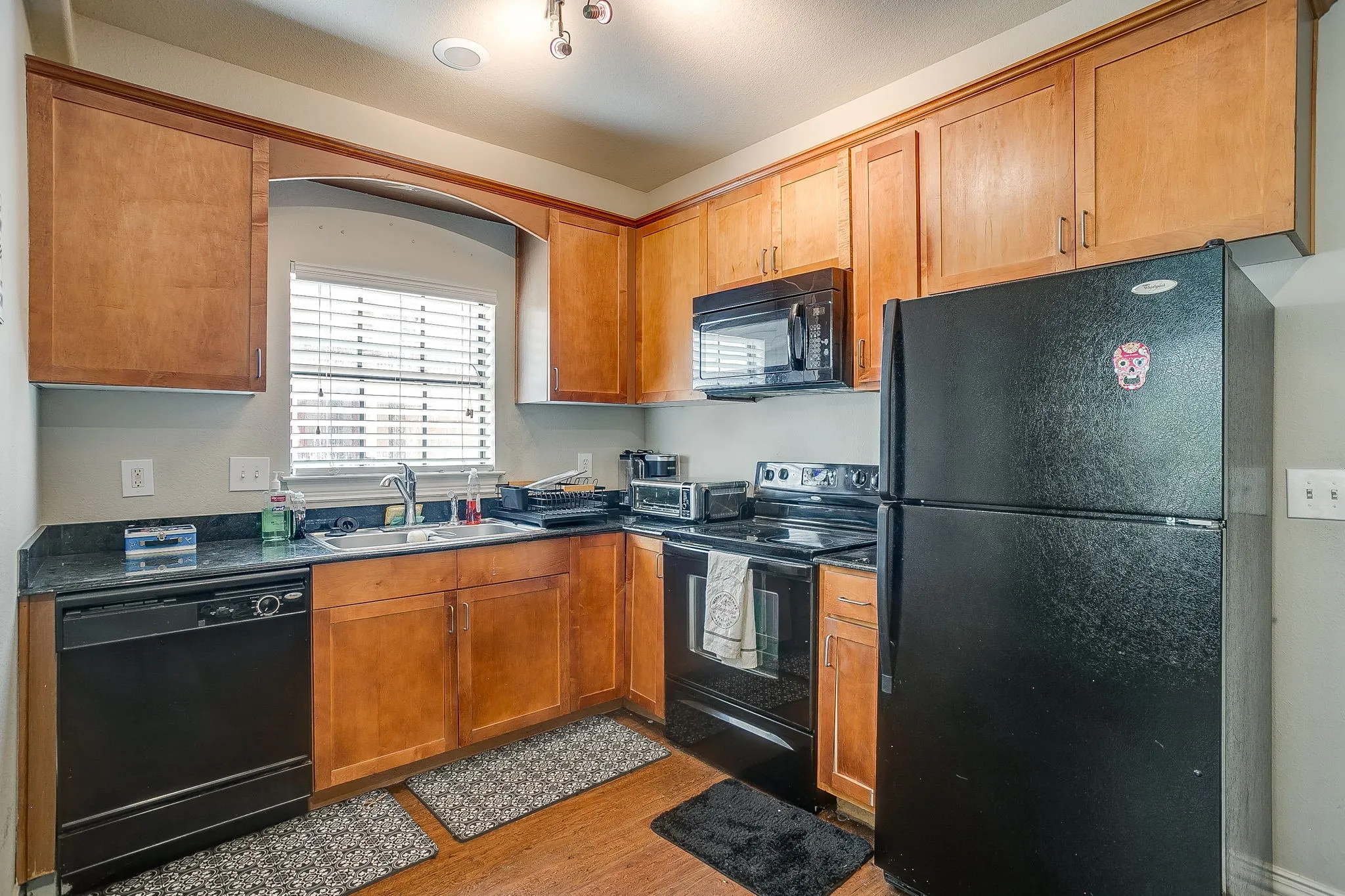 Kitchen with black appliances, wood finish cabinets, and light wood finished floors