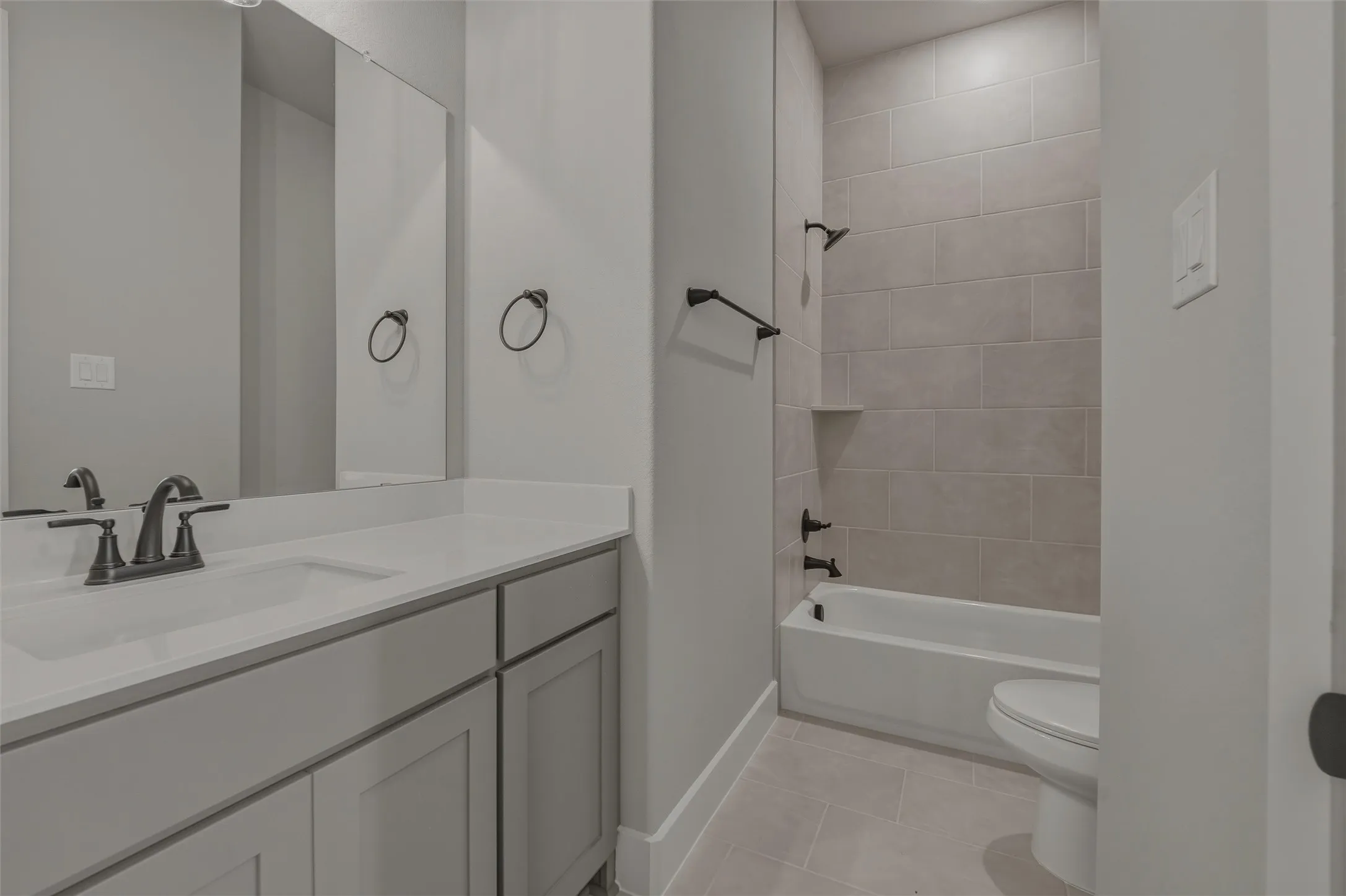 Bathroom featuring a white vanity with an integrated sink and dark bronze fixtures, a framed mirror, and light gray cabinetry