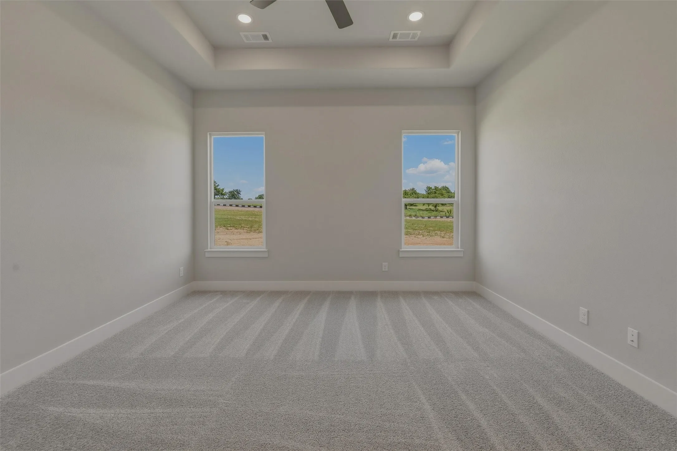 Spacious room featuring a tray ceiling with recessed lighting and a ceiling fan