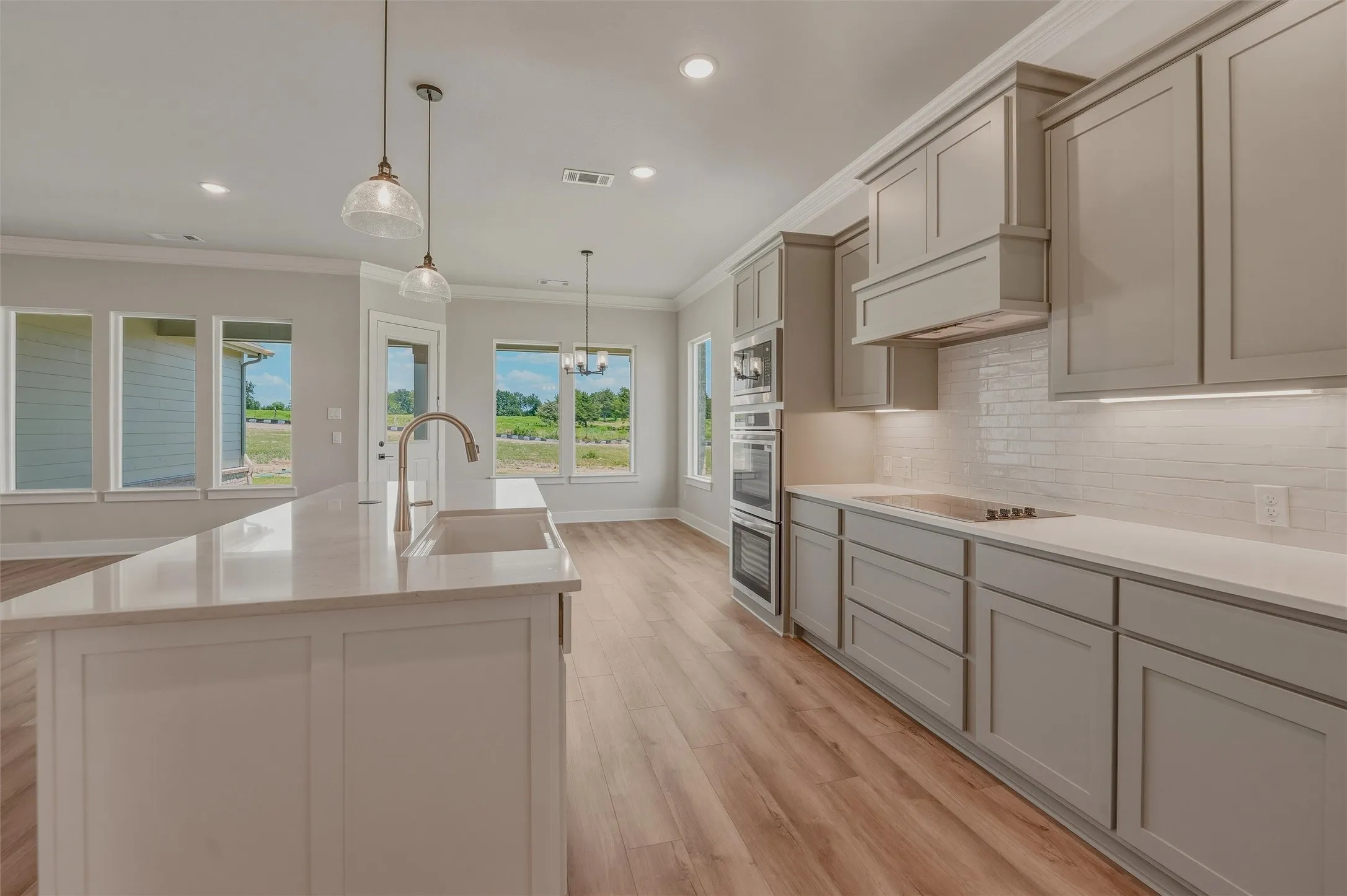 Modern kitchen featuring a large island with an undermount sink, light-toned cabinetry, integrated double ovens, and wood-finish flooring