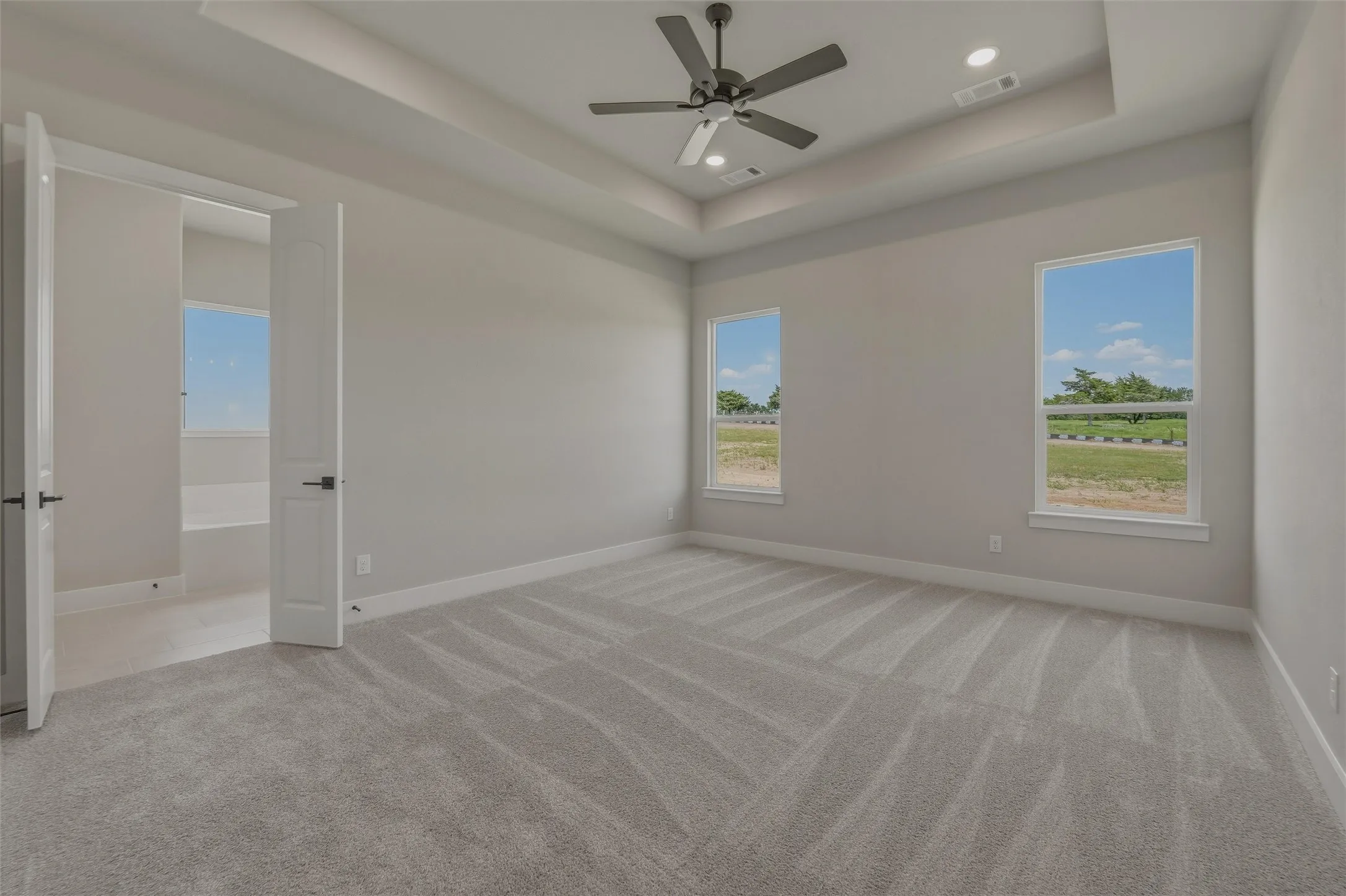 Spacious room featuring tray ceiling, recessed lighting, ceiling fan, carpeting, and two windows