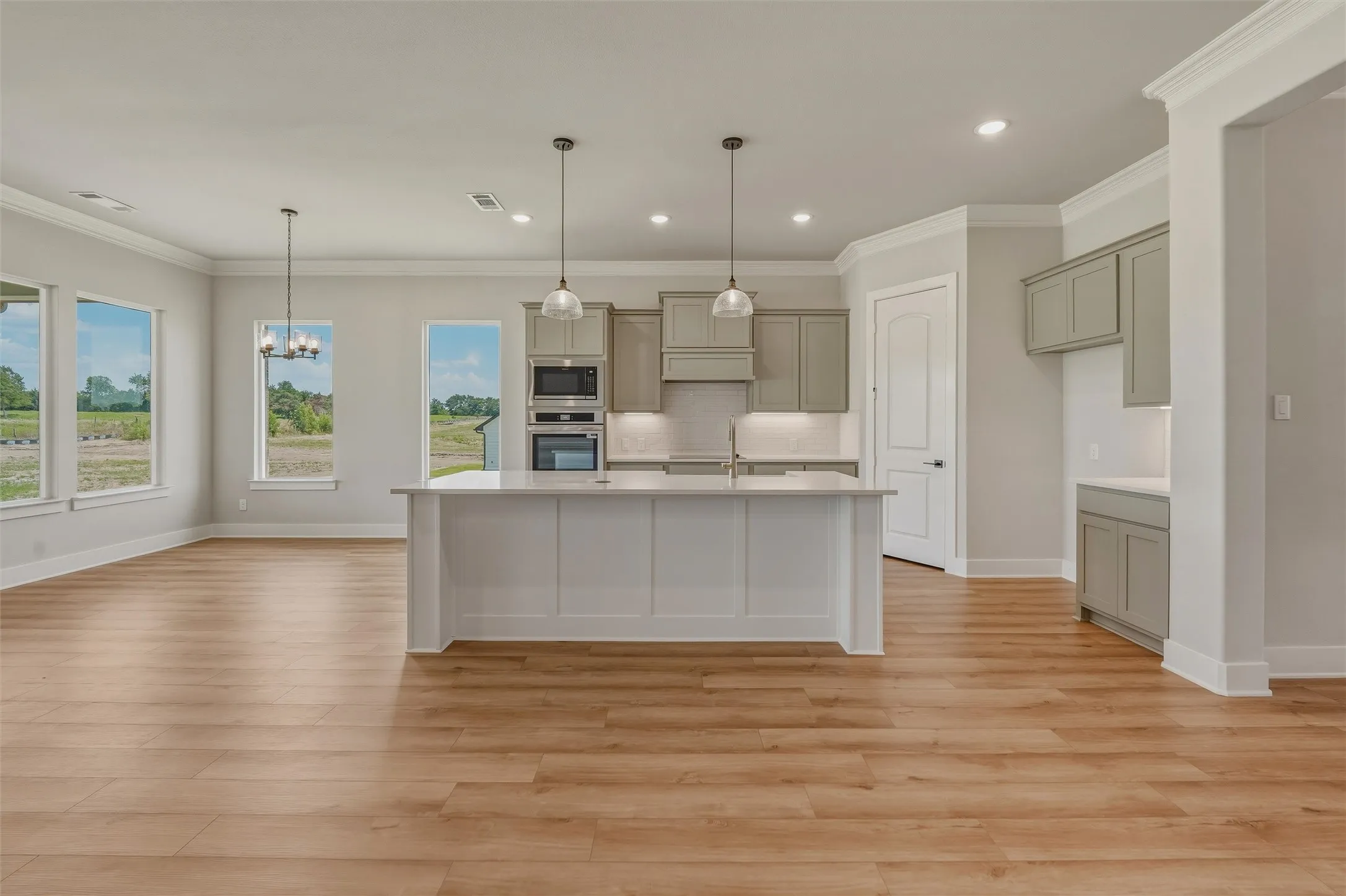 Open-concept living space featuring wood-finish flooring, a kitchen island with pendant lighting, stainless steel appliances, recessed lighting, and multiple windows