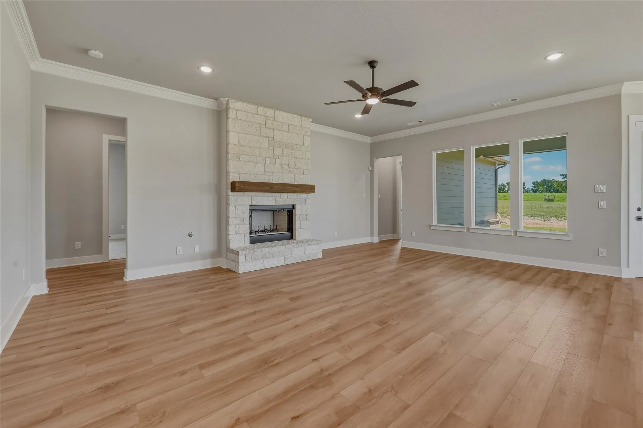 Spacious room featuring wood-finish flooring, a stone fireplace with a wood mantel, a ceiling fan, recessed lighting, and multiple windows