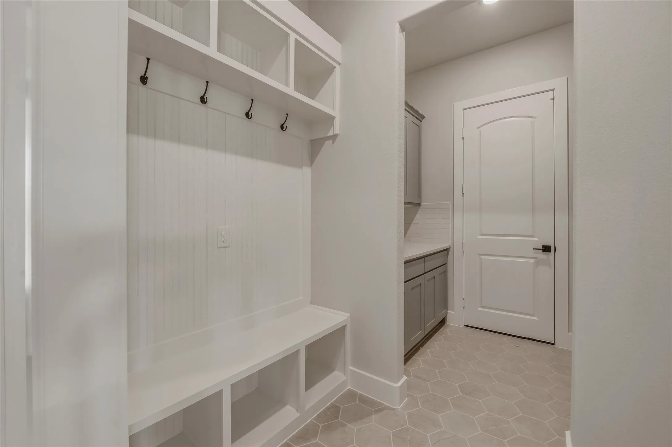 Built-in mudroom bench with storage cubbies and upper shelving, featuring beadboard paneling and coat hooks