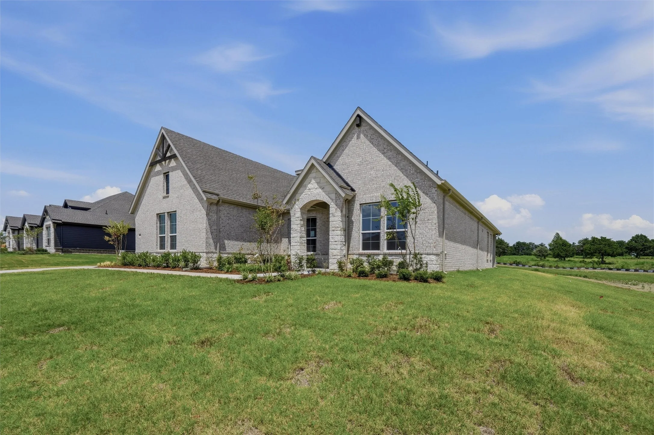Contemporary-style home featuring light gray brick veneer, a dark shingle roof, and an arched entry