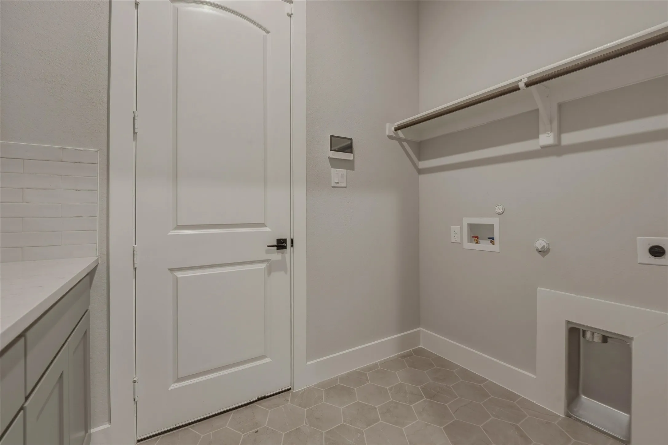 Dedicated laundry space featuring hexagonal floor tiling, a utility sink, and built-in shelving with a hanging rod