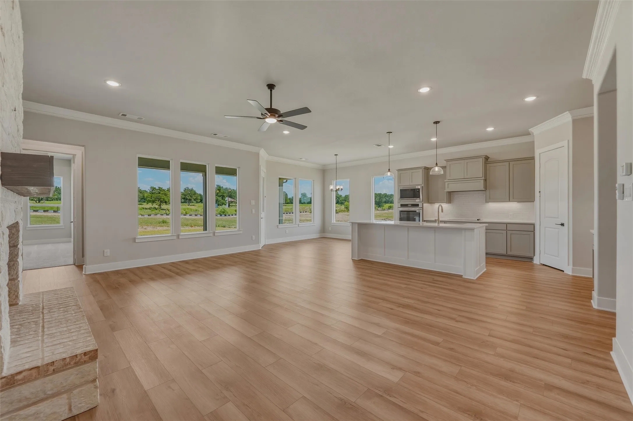 Expansive open-concept living area featuring wood-finish flooring, a contemporary kitchen island with pendant lighting, a built-in double oven, and recessed lighting