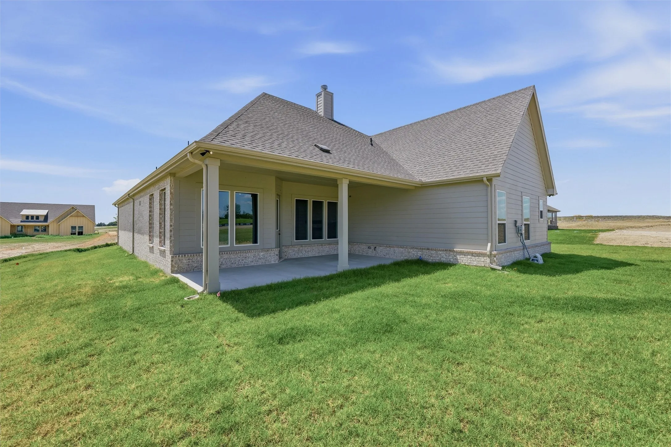 Rear exterior with covered patio, featuring a gabled roofline, siding, brick wainscoting, and multiple windows