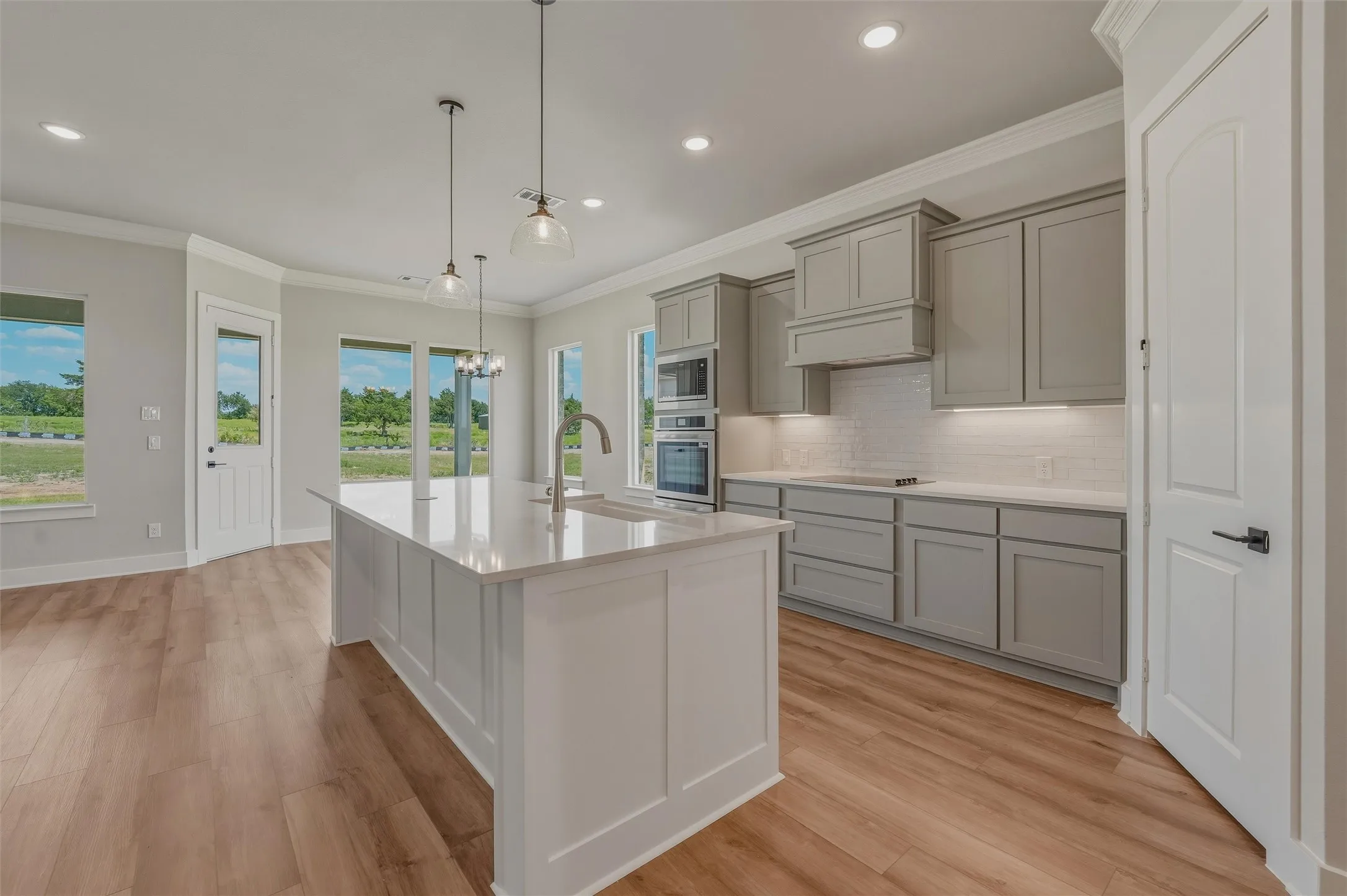 Gourmet kitchen featuring a central island with countertop seating, light gray cabinetry, built-in double ovens, and a subway tile backsplash