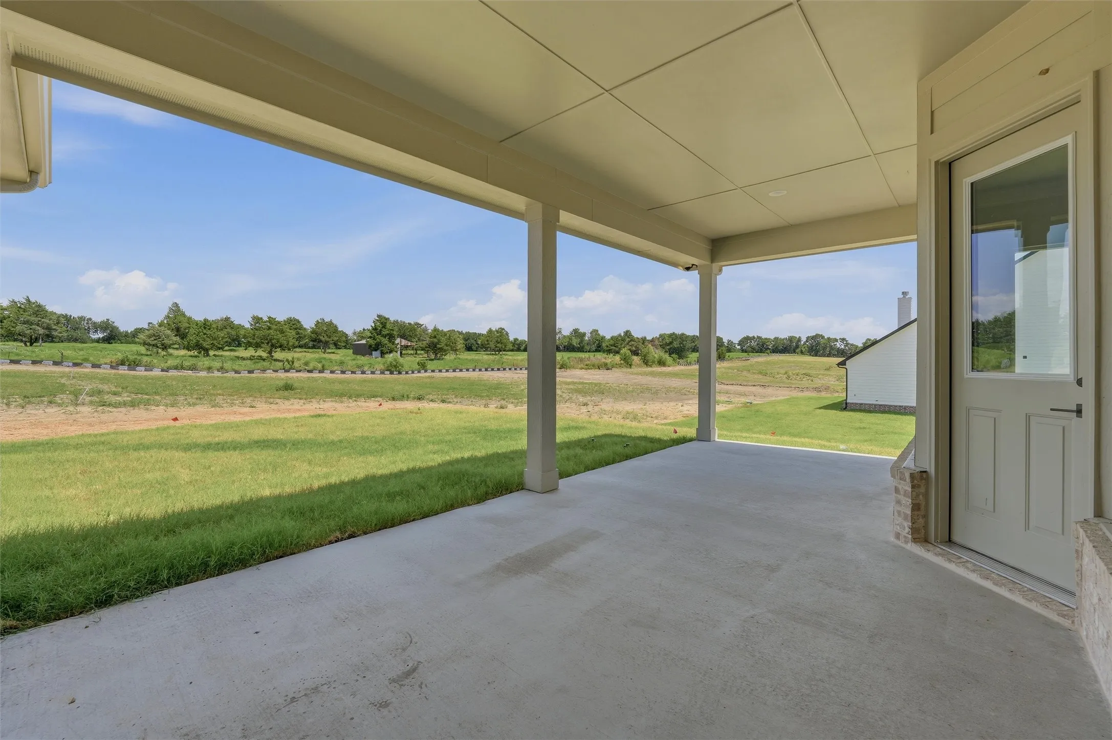 Spacious covered patio with a concrete surface, supported by columns, offering expansive views of undeveloped land and a distant tree line
