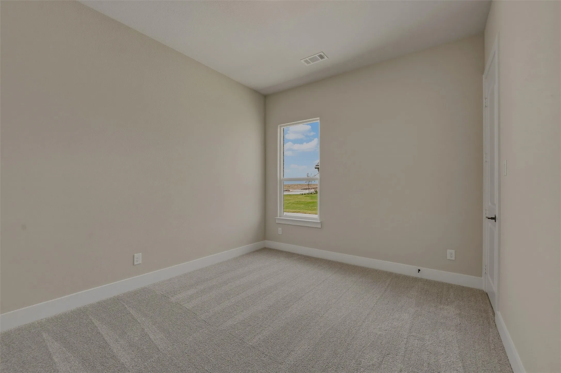 Neutral tone wall paint, light-colored carpeting, white baseboards, and a single window with white trim