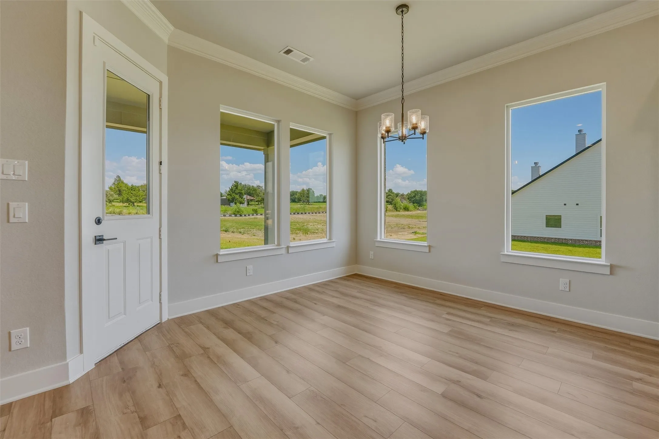 Spacious interior with wood-finish flooring, multiple windows, a ceiling-mounted light fixture, and crown molding