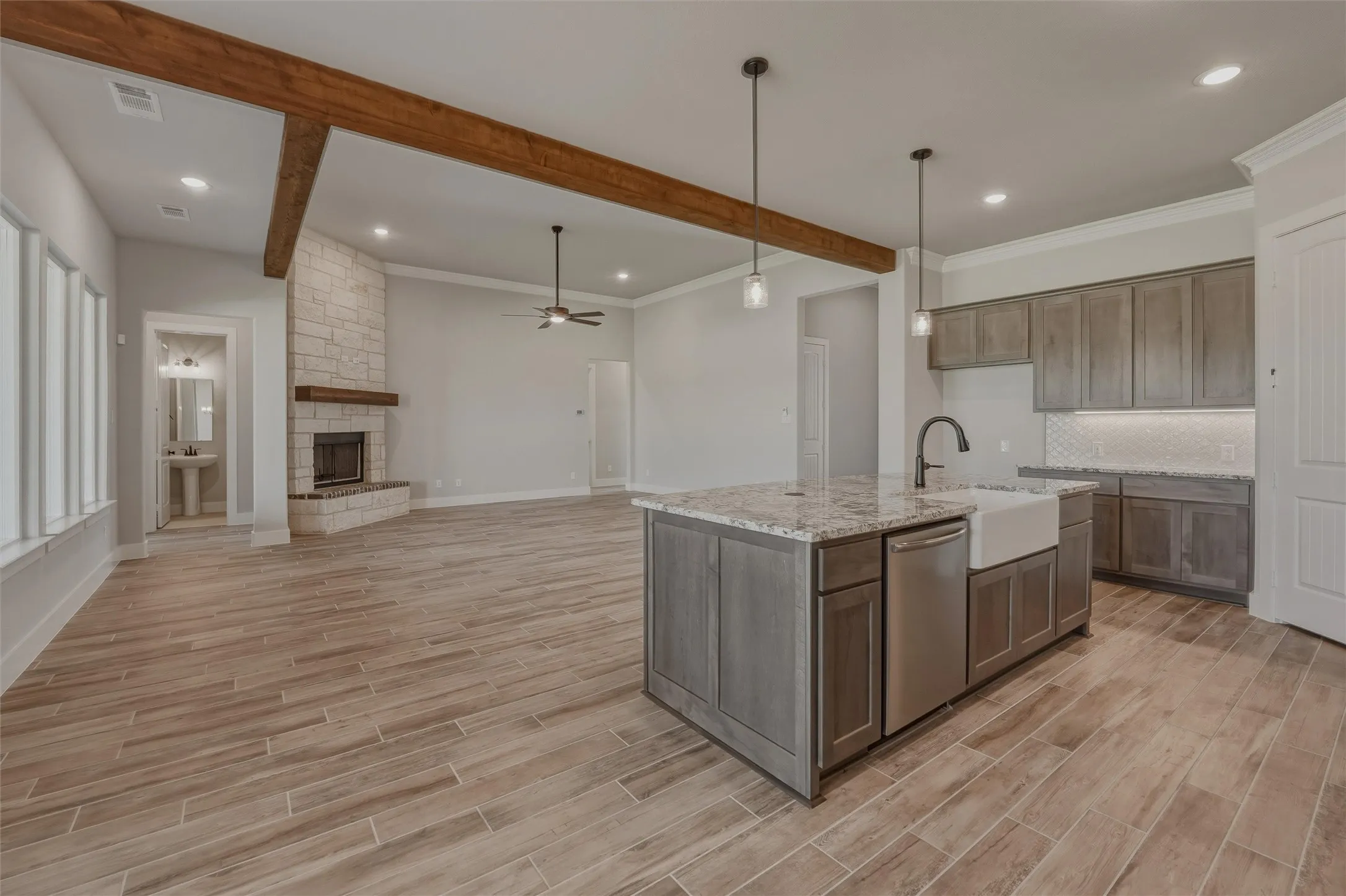 Open-concept living space featuring wood-finish flooring, exposed ceiling beams, and a stone fireplace with a wood mantel