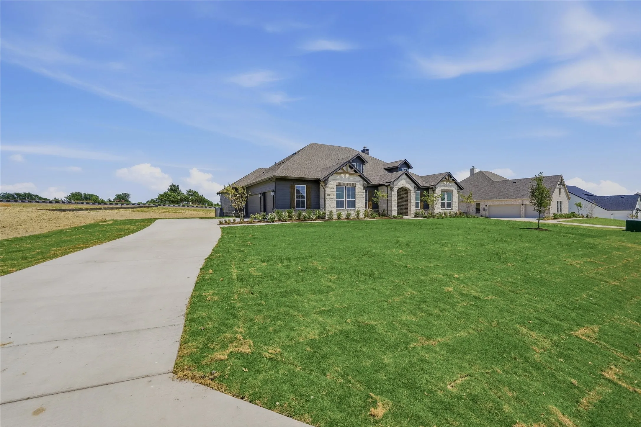 Expansive front lawn with a concrete driveway leading to a stone and siding exterior