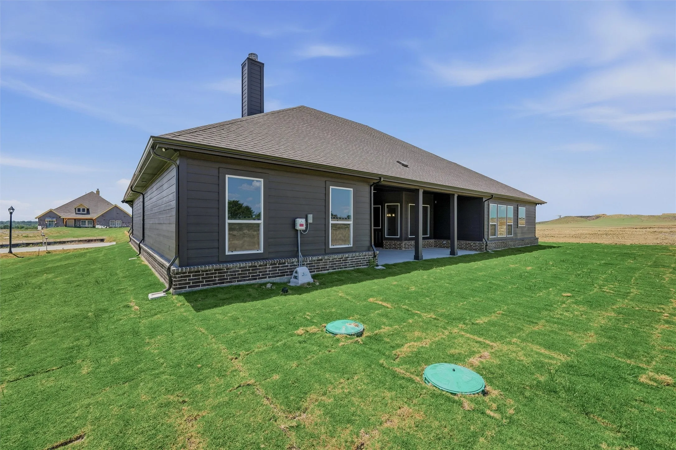 Rear exterior featuring dark horizontal siding, a stone accent base, and a covered patio with supporting columns