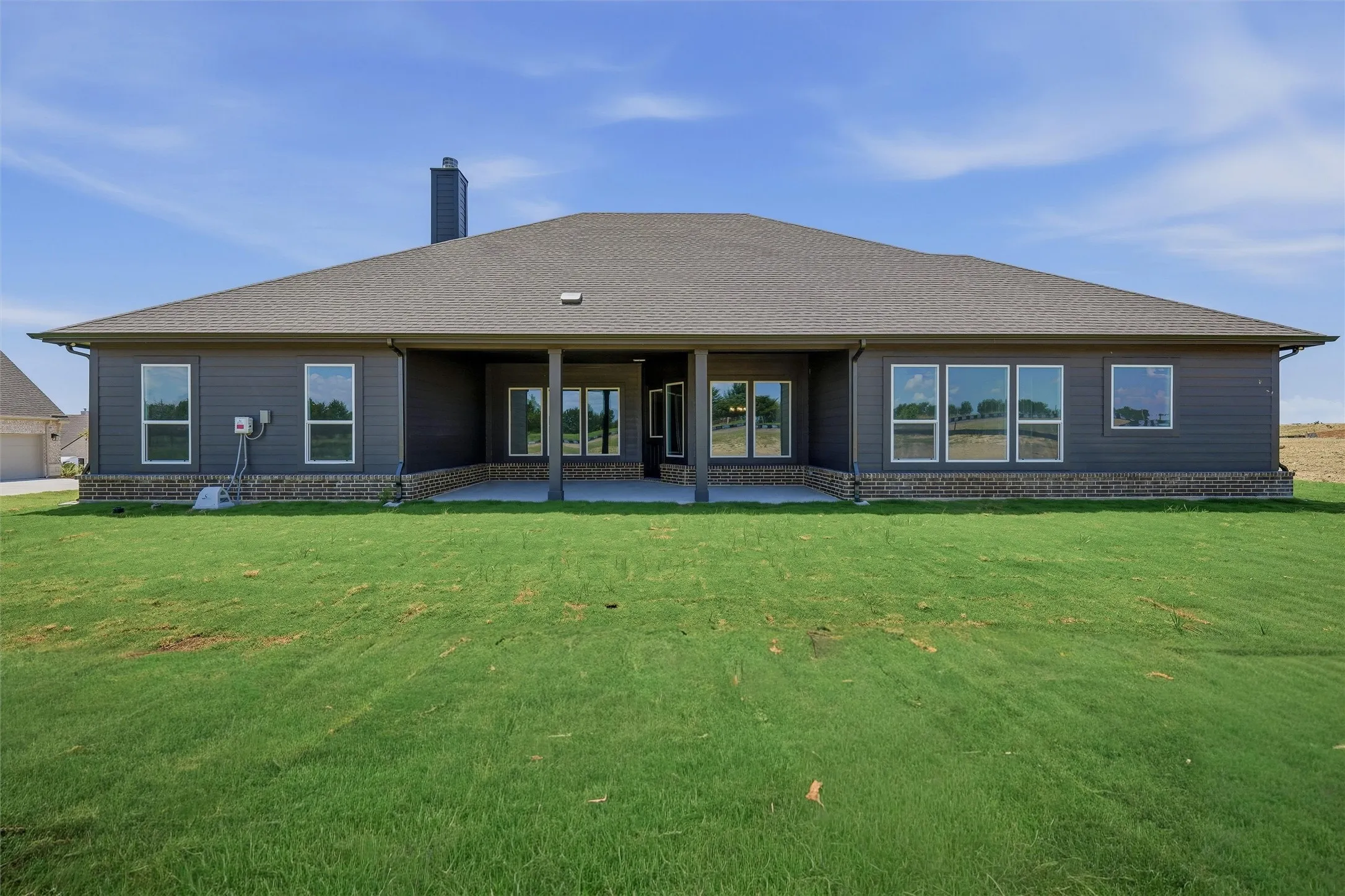 Contemporary rear exterior featuring dark gray siding and stone wainscoting