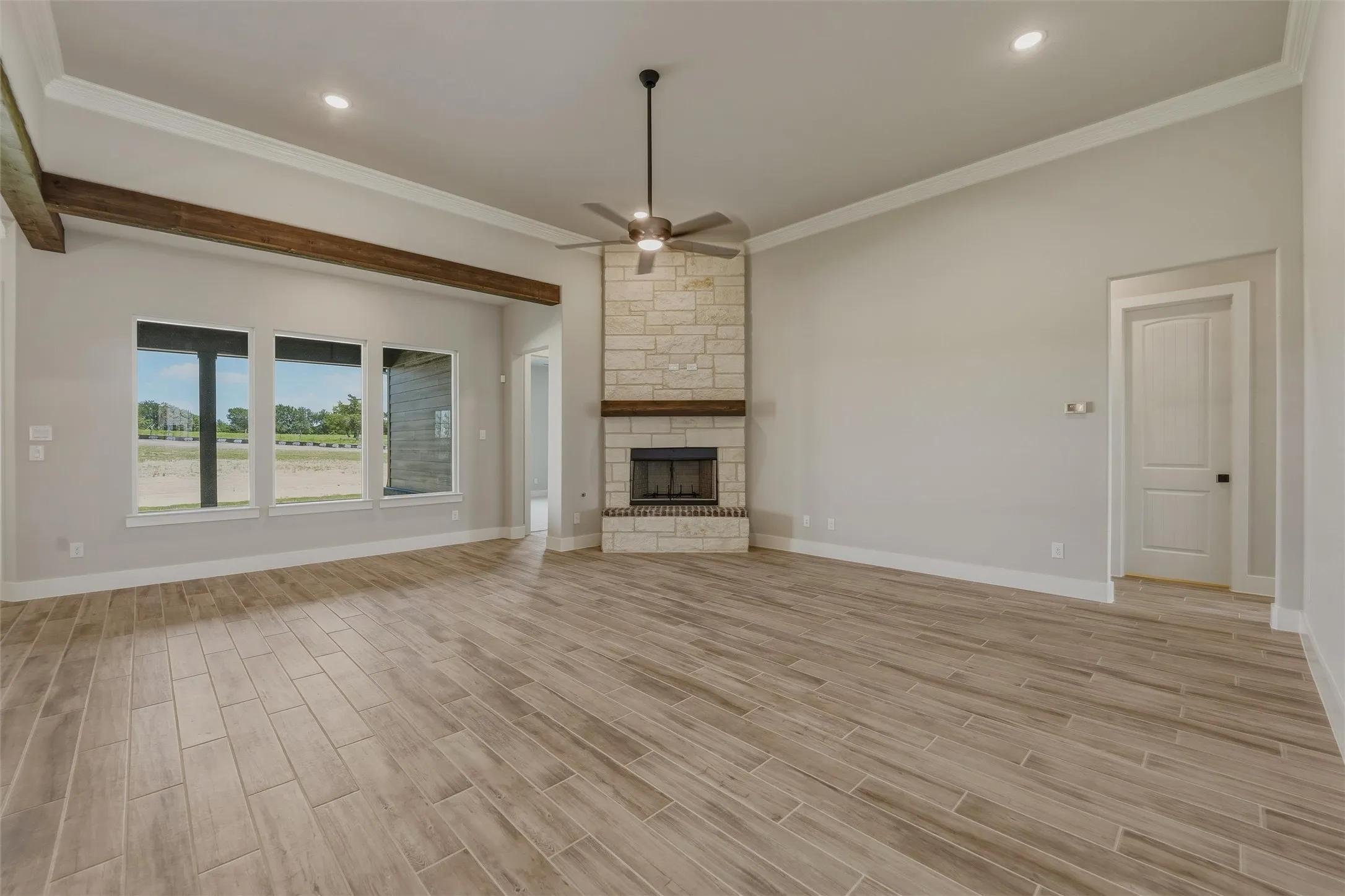 Spacious room featuring wood-finish flooring, a stone fireplace with a wood mantel, and multiple windows