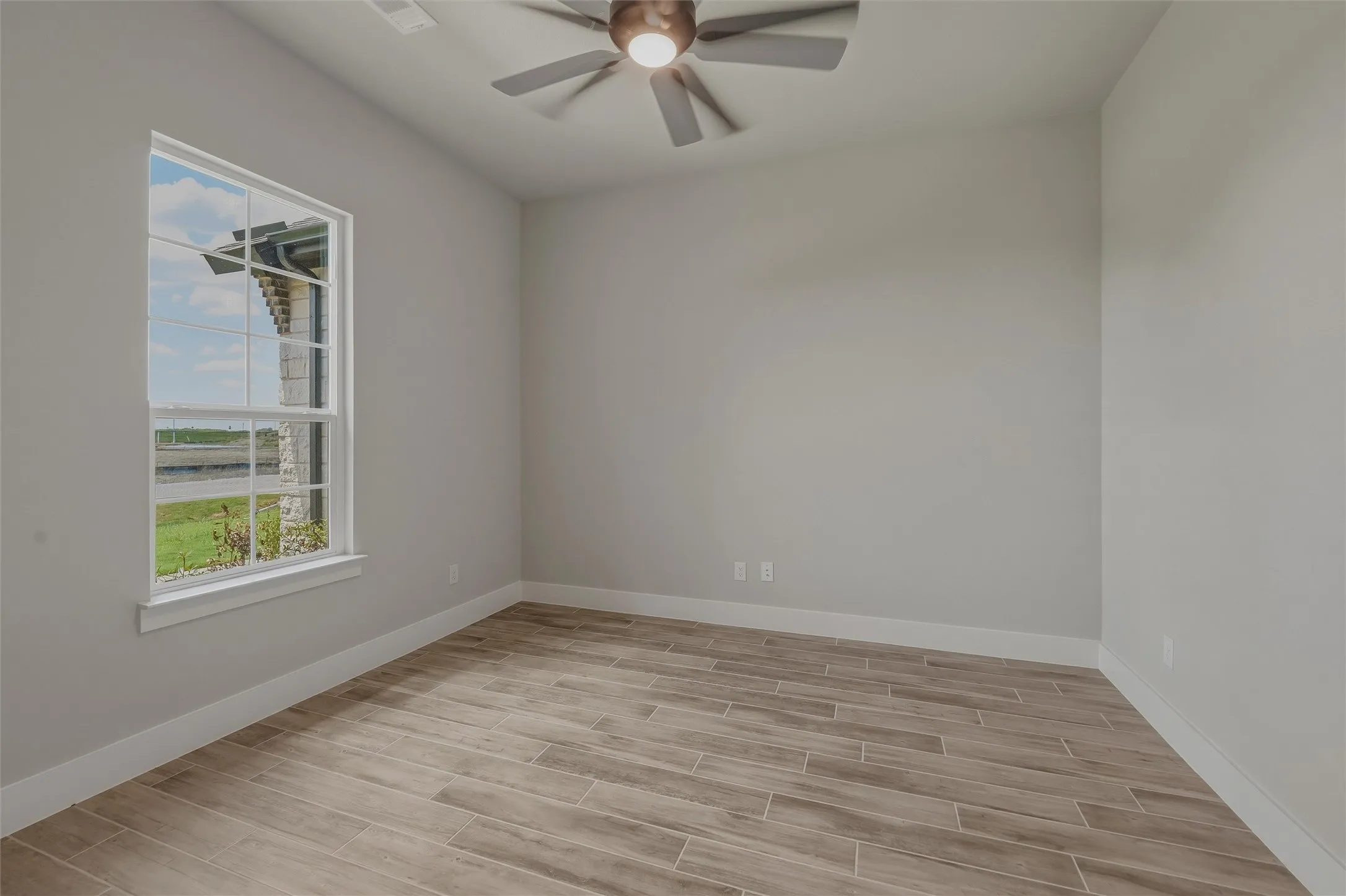 Room featuring a large window, light-toned walls, wood-finish flooring, white baseboards, and a ceiling fan