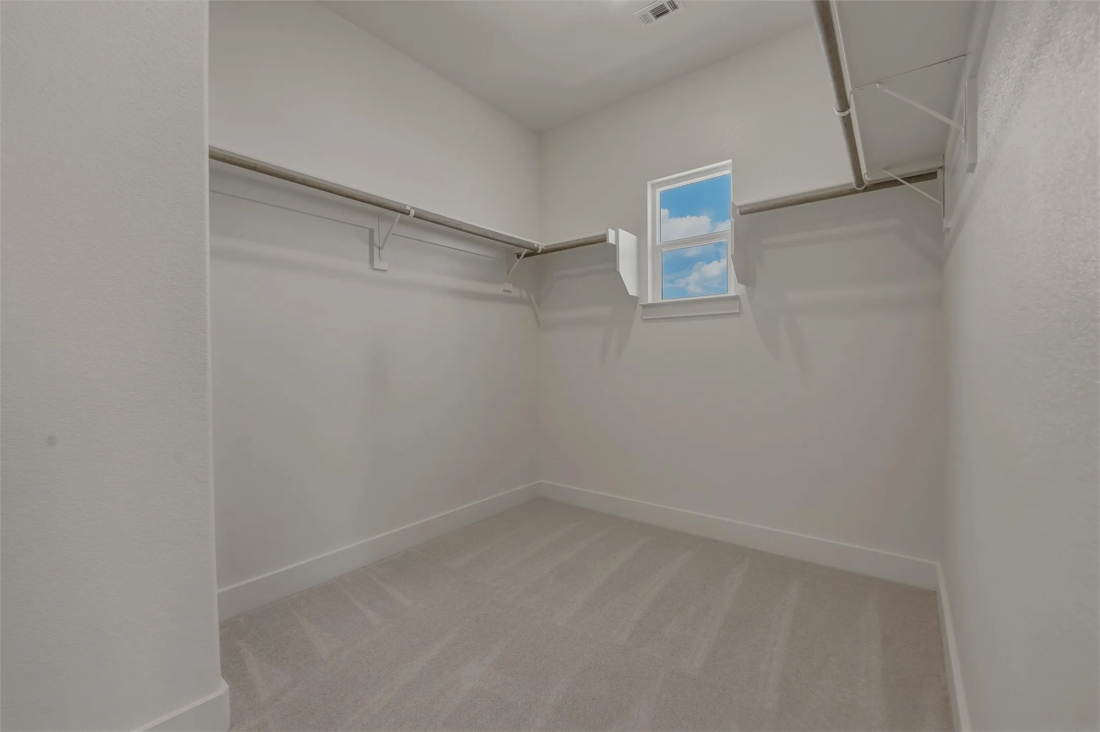 Spacious walk-in closet featuring light-toned carpeting, white walls, and built-in shelving with hanging rods