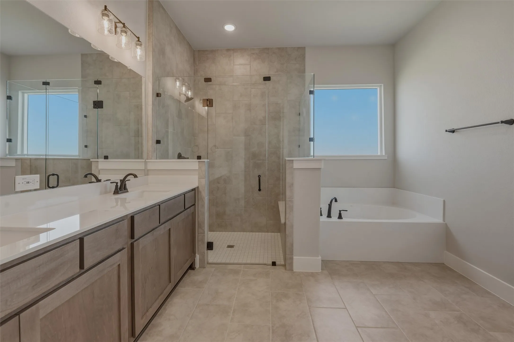 Spacious bathroom featuring a dual vanity with a light-toned countertop, a walk-in shower with clear glass enclosure and tiled walls, a built-in soaking tub, and large format floor tiles