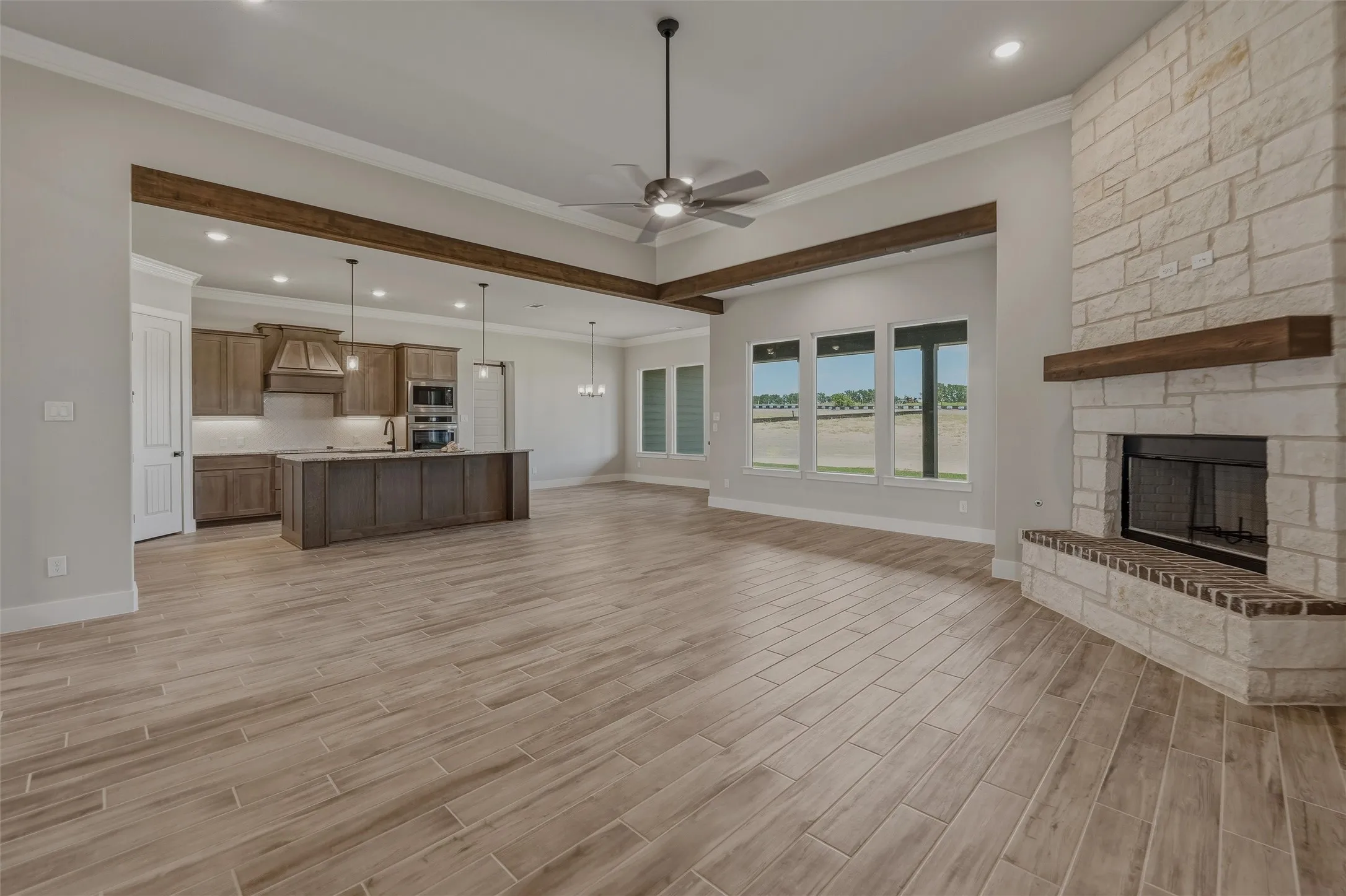 Spacious living area featuring wood-finish flooring, a stone fireplace with a wood mantle, and an open concept kitchen