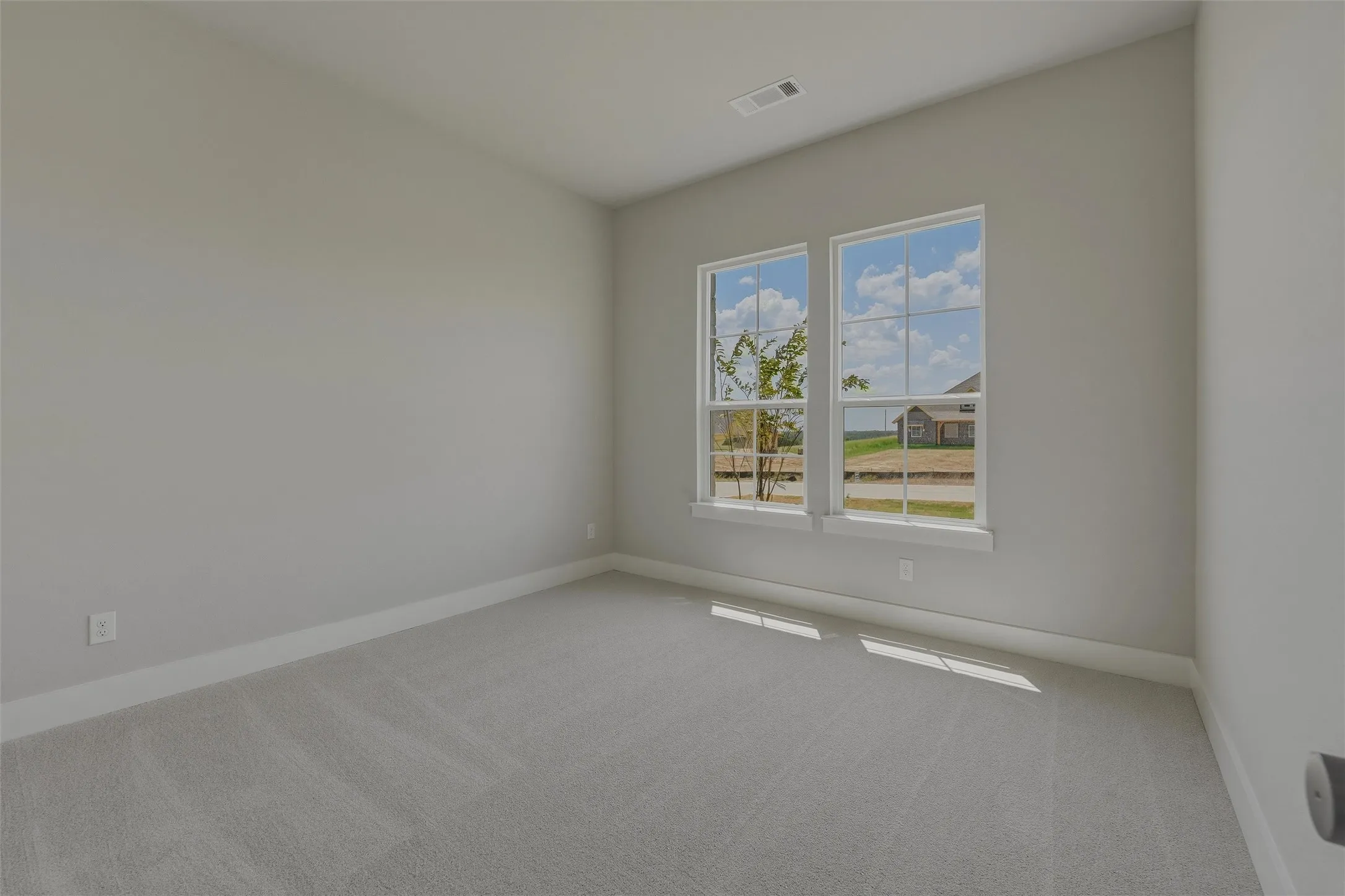 Carpeted room featuring two prominent windows, sloped ceiling, and neutral wall paint