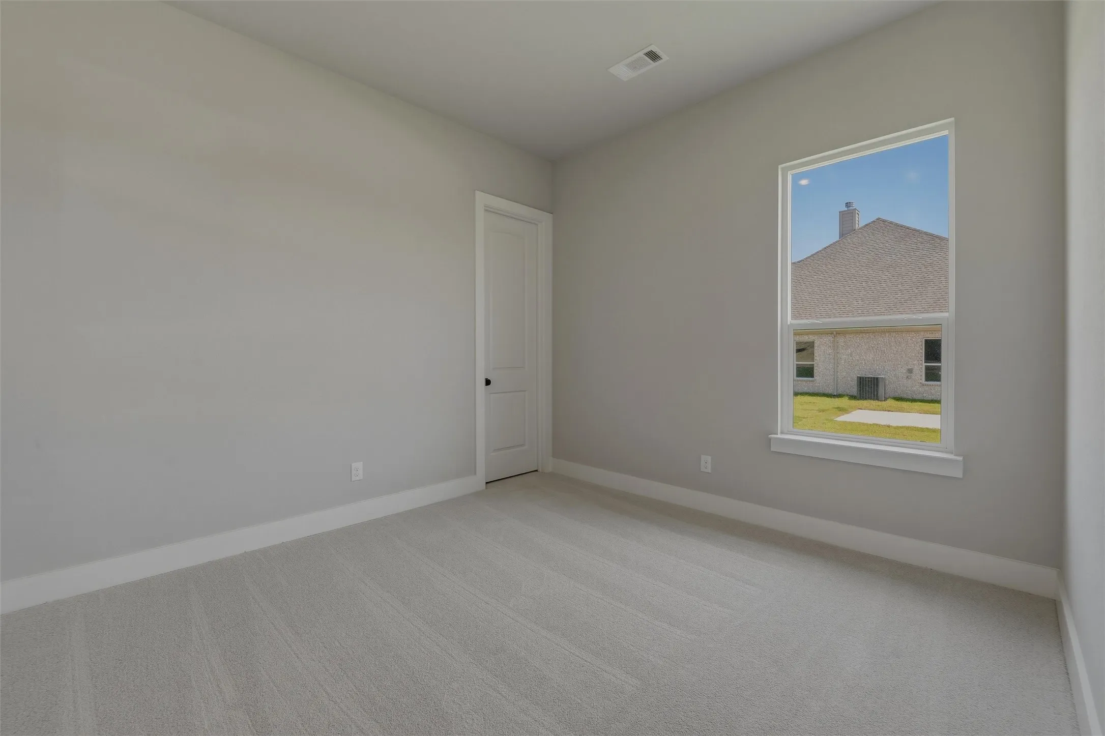 Neutral gray wall paint with white trim, light gray carpet, a white interior door with black hardware, and a single pane window