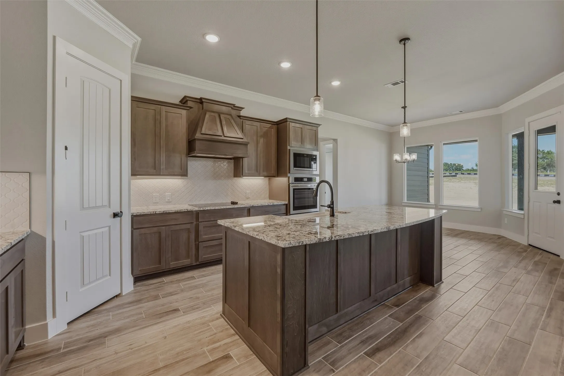 Kitchen featuring a large island with a stone countertop, built-in stainless steel appliances, wood-finish cabinetry, a decorative range hood, and wood-finish flooring