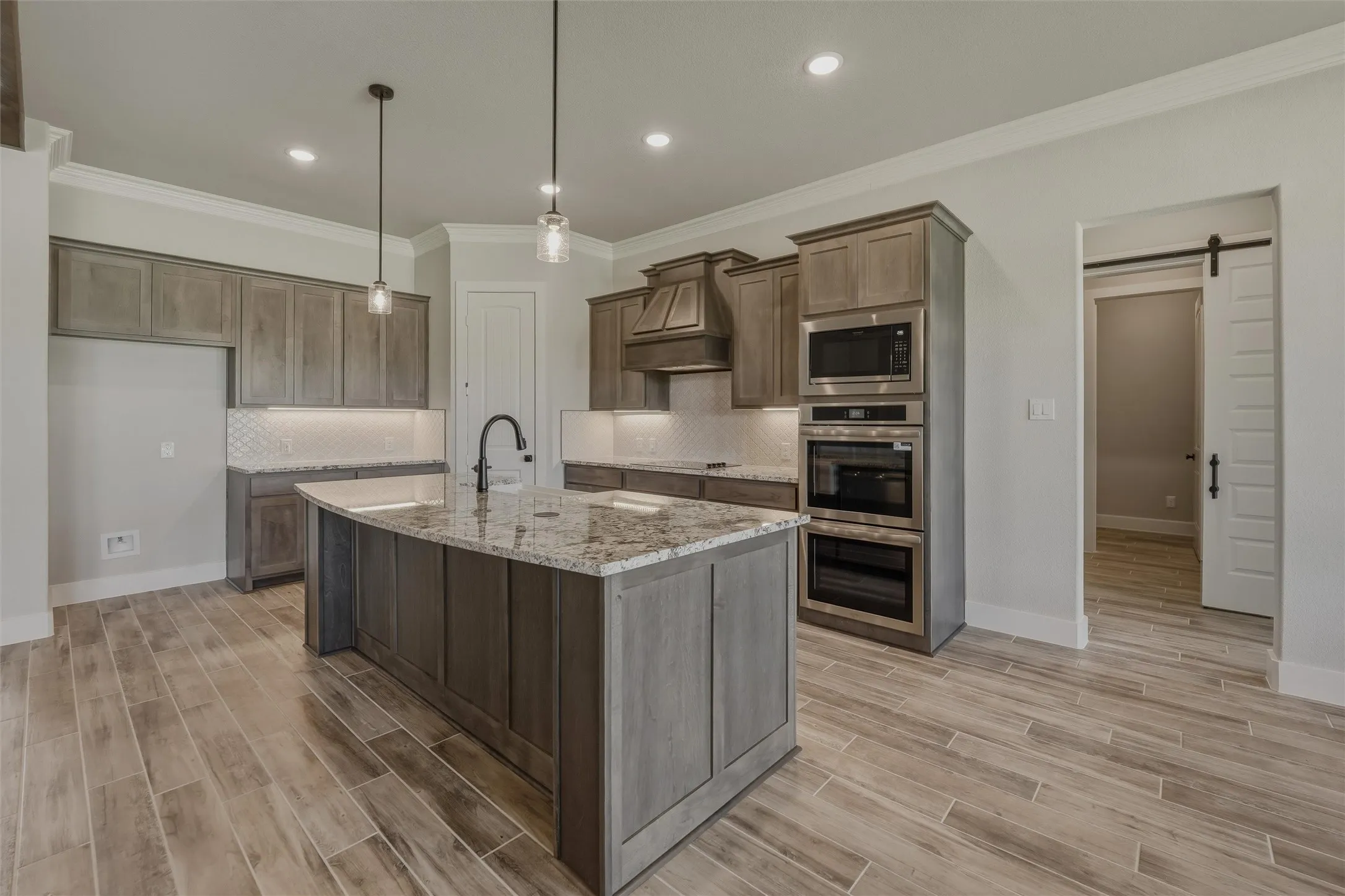 Kitchen featuring a central island with a granite countertop, wood-finish flooring, recessed lighting, pendant lights, a built-in microwave, and double ovens