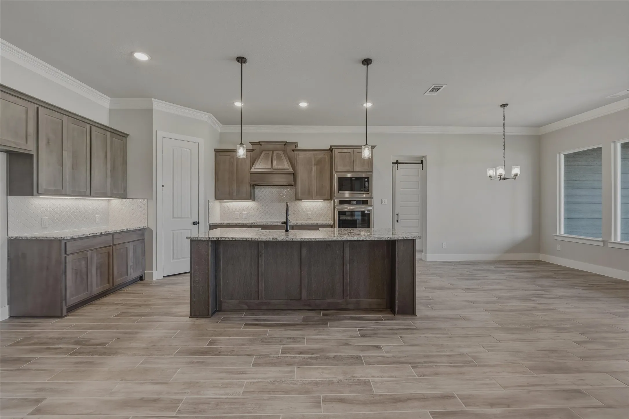 Spacious kitchen featuring an expansive island with pendant lighting, wood-finish cabinetry, integrated wall ovens, a tile backsplash, and wood-finish tile flooring