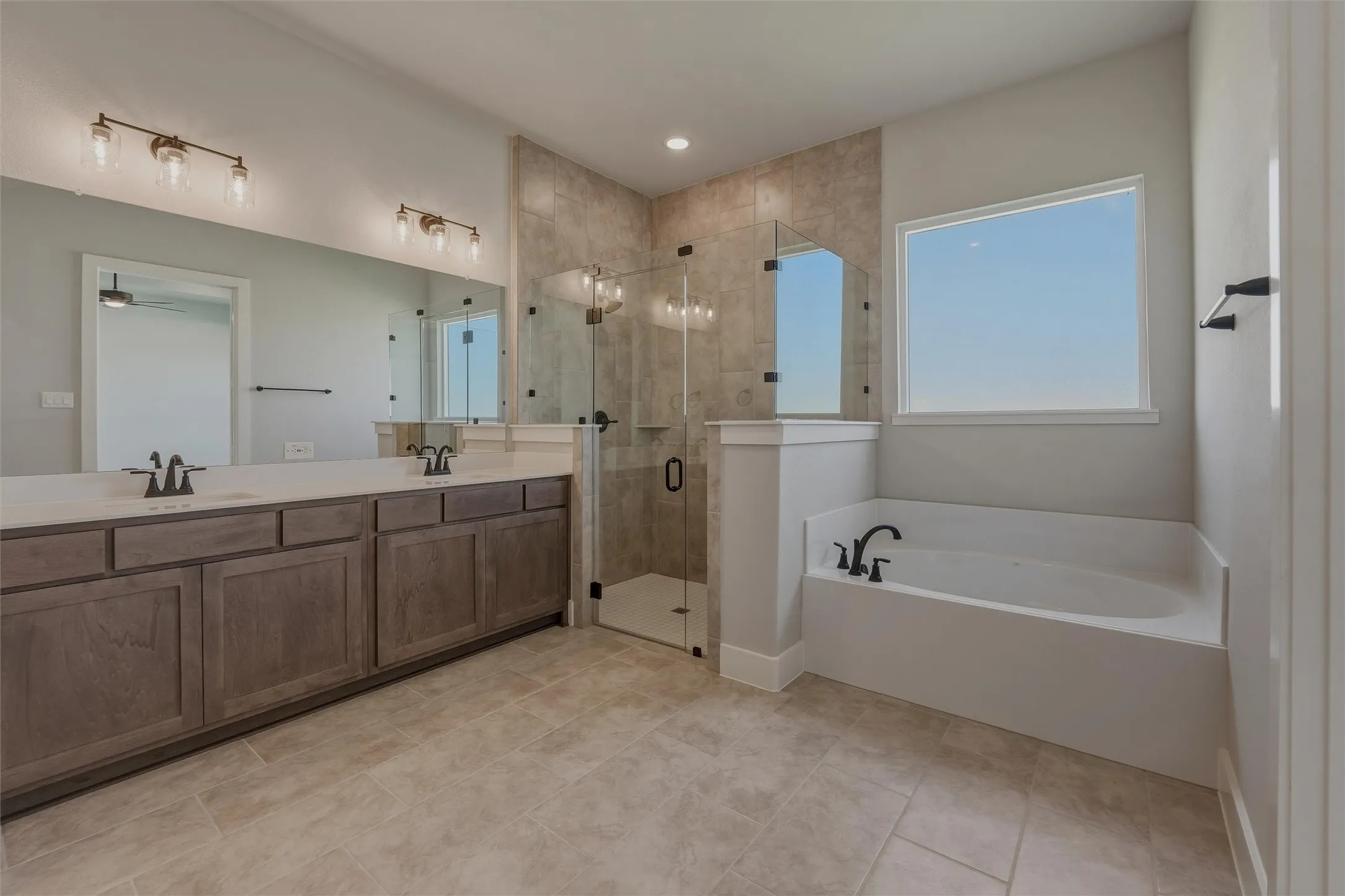 Spacious bathroom featuring a dual vanity with a light-colored countertop, a tiled walk-in shower with a glass enclosure, a built-in soaking tub, and neutral-toned tile flooring