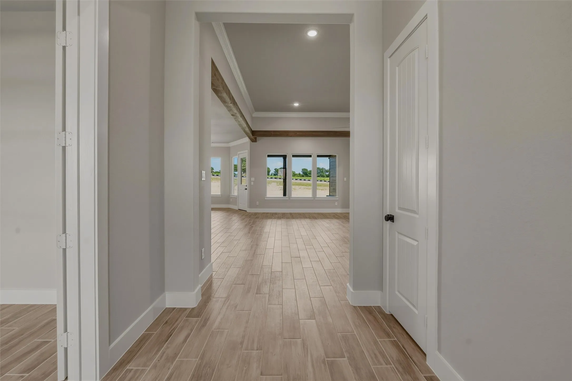 Hallway entrance leading to an expansive open-concept living area with wood-finish flooring, recessed lighting, exposed ceiling beams, and a bay window featuring multiple panes