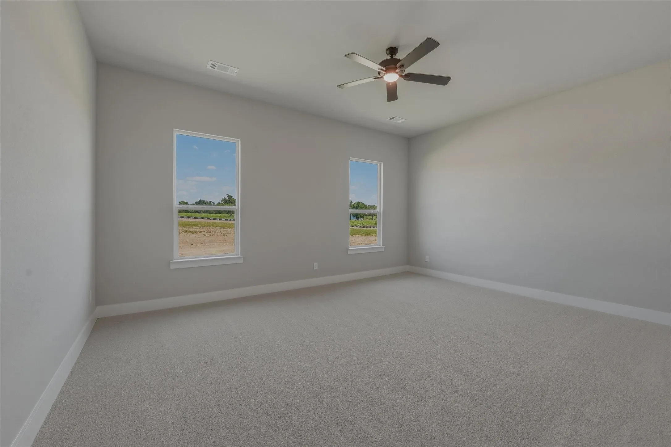 Spacious room featuring neutral carpeting, light gray walls, a ceiling fan with integrated lighting, and two windows providing natural light