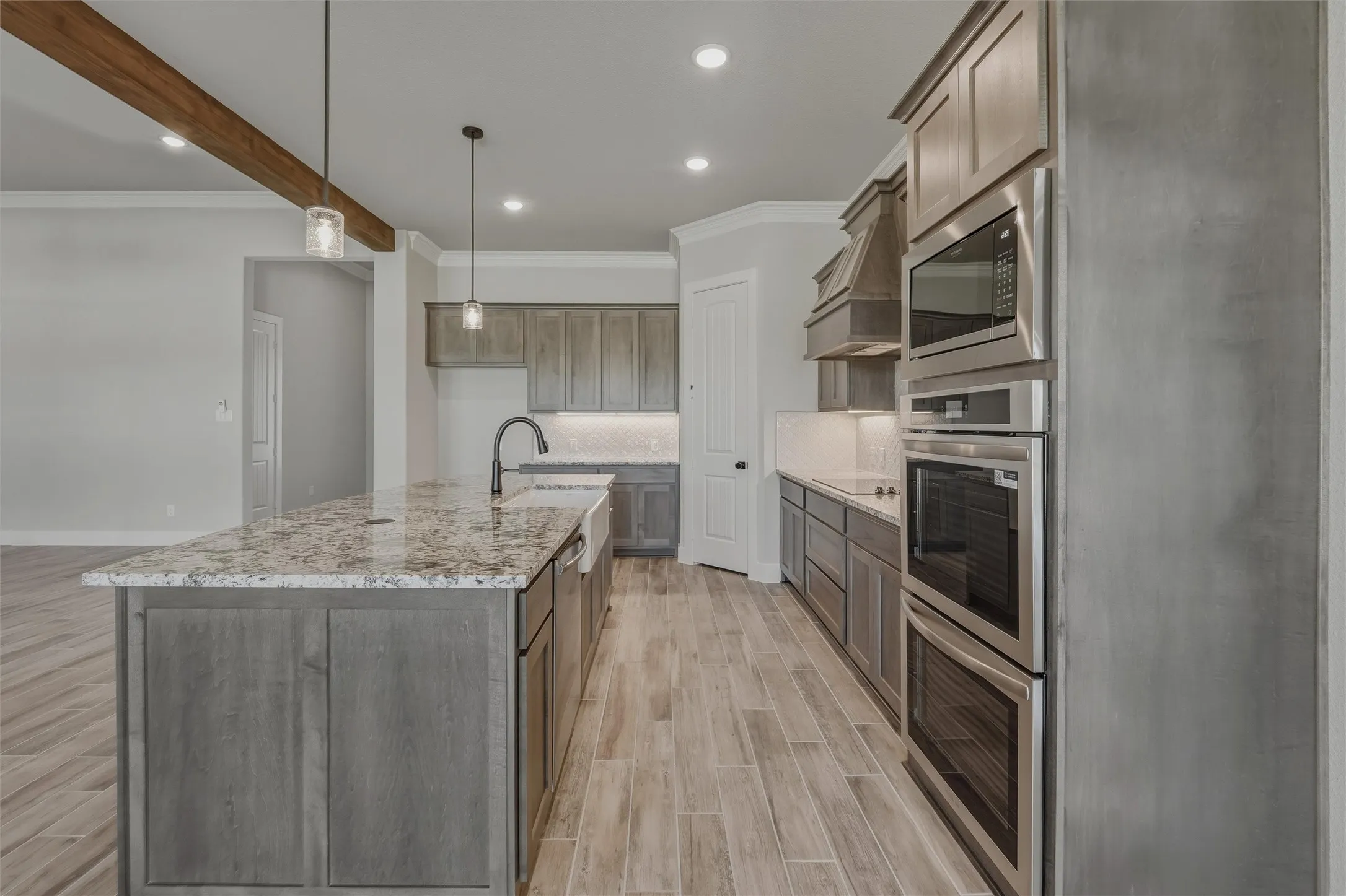 Kitchen featuring an expansive island with a light-toned countertop, wood-finish flooring, built-in stainless steel appliances, a farmhouse sink, and pendant lighting