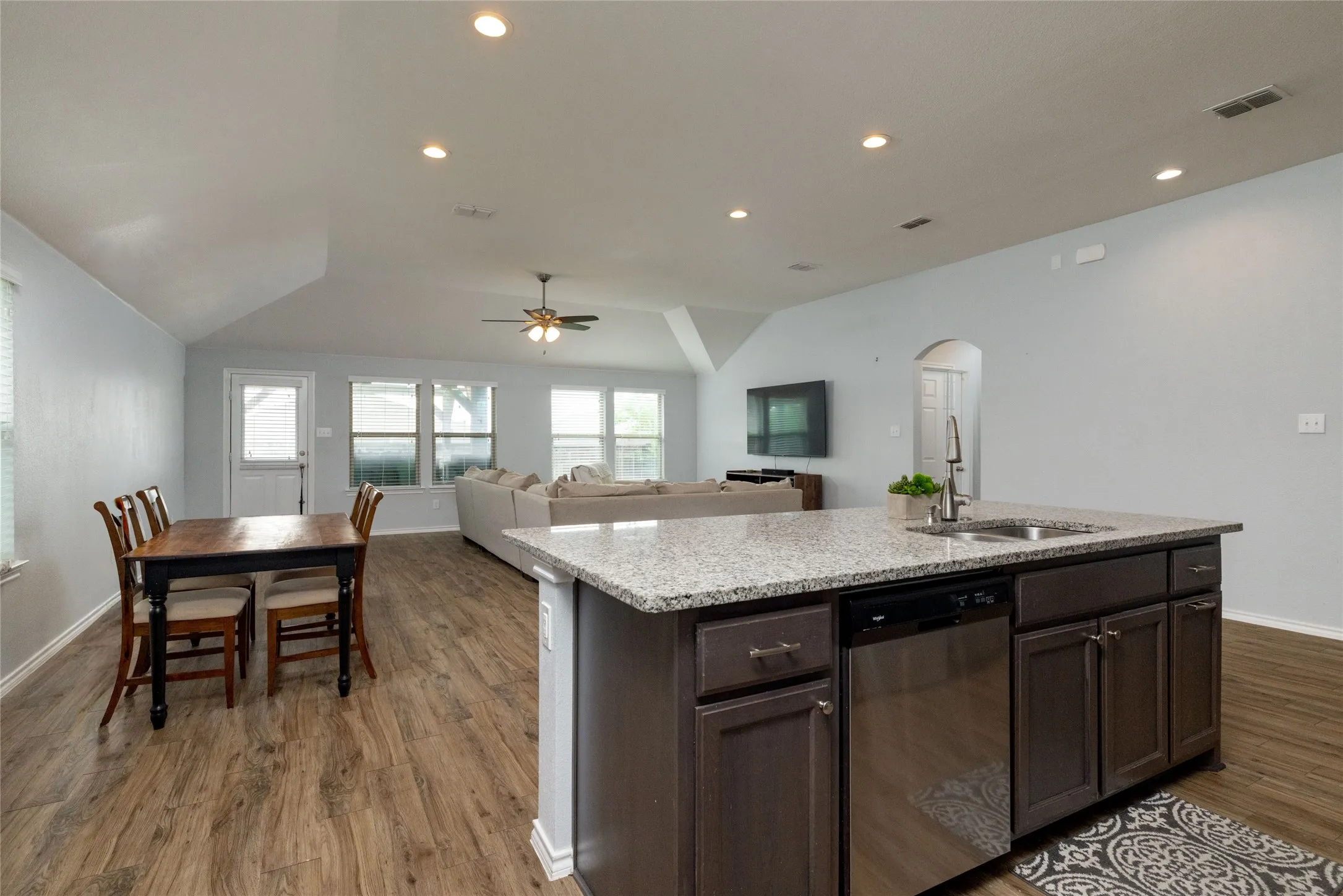 Kitchen featuring dark wood finish cabinets, dishwasher, open floor plan, a center island with sink, and a ceiling fan