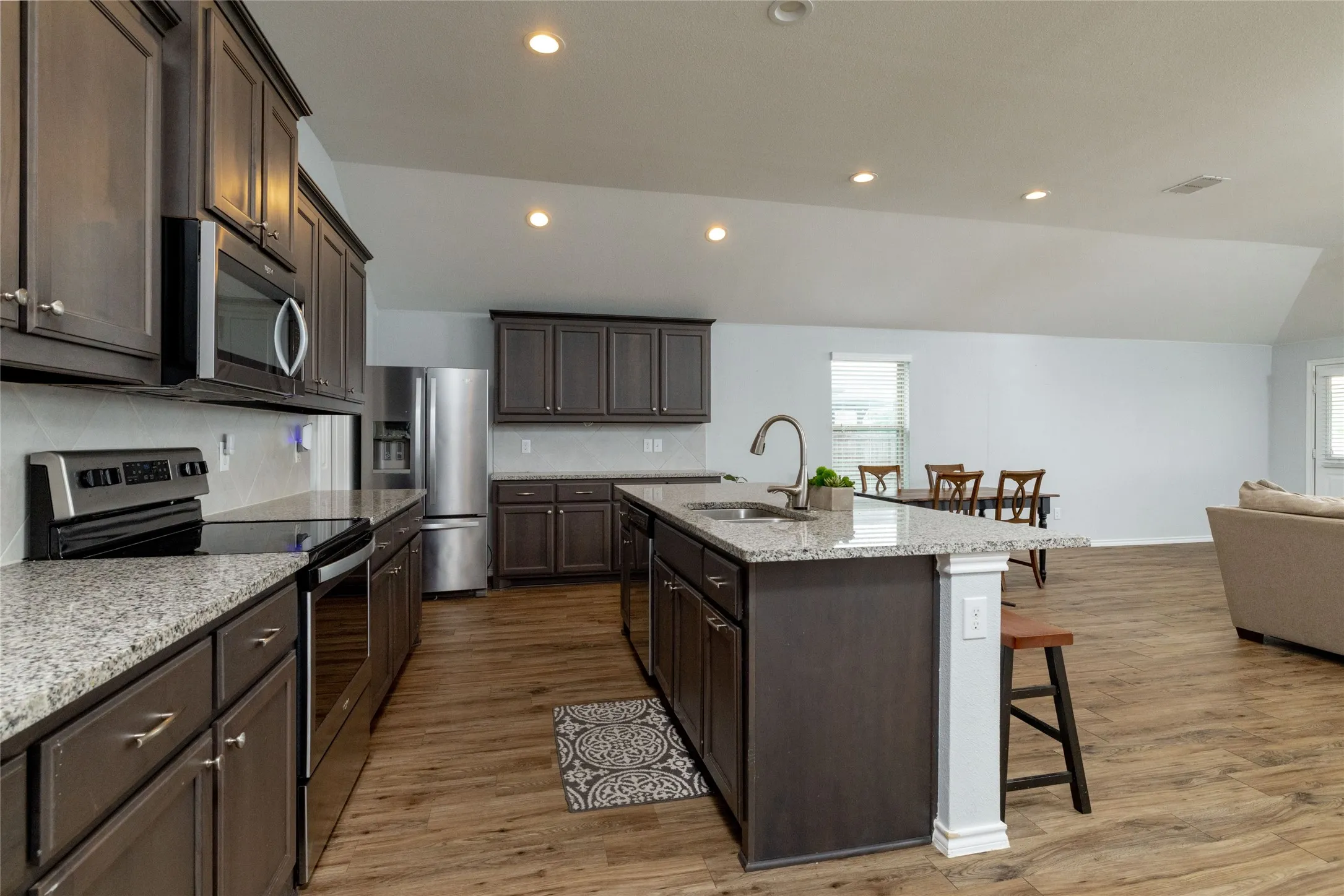 Kitchen featuring stainless steel appliances, light stone counters, decorative backsplash, an island with sink, and light wood-type flooring