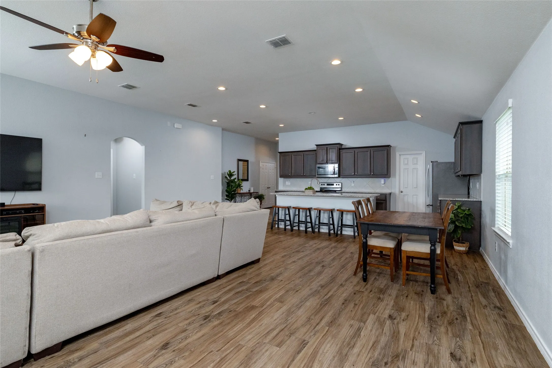 Living area with arched walkways, light wood-style floors, ceiling fan, lofted ceiling, and recessed lighting